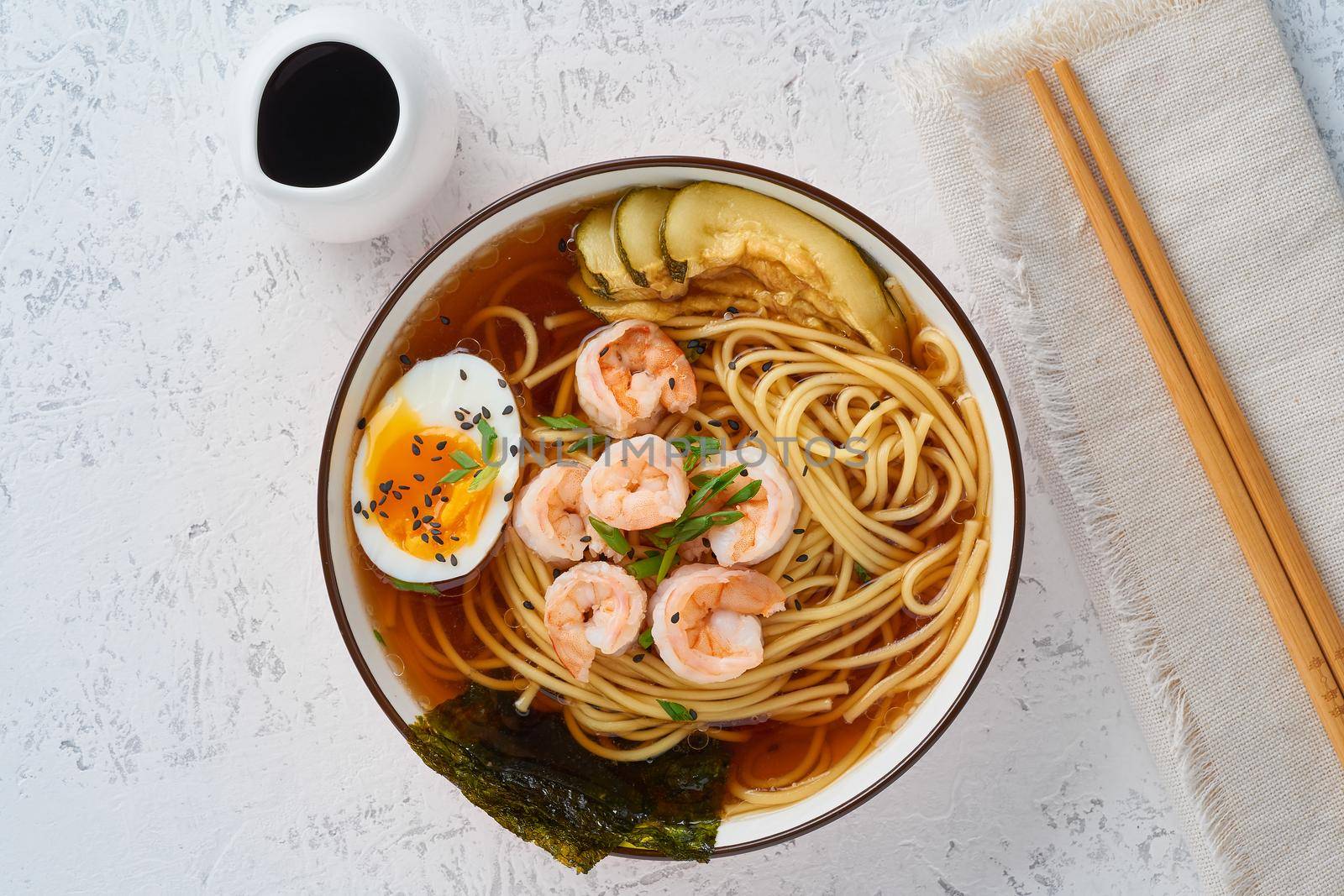 Asian soup with a noodles, ramen with shrimps, miso paste, soy sauce. White stone table