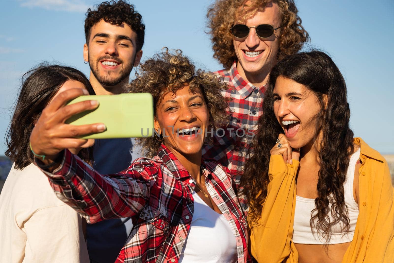 Smiling young multiracial friends take selfie together using smartphone outdoors. Having fun. Friendship and technology concept.