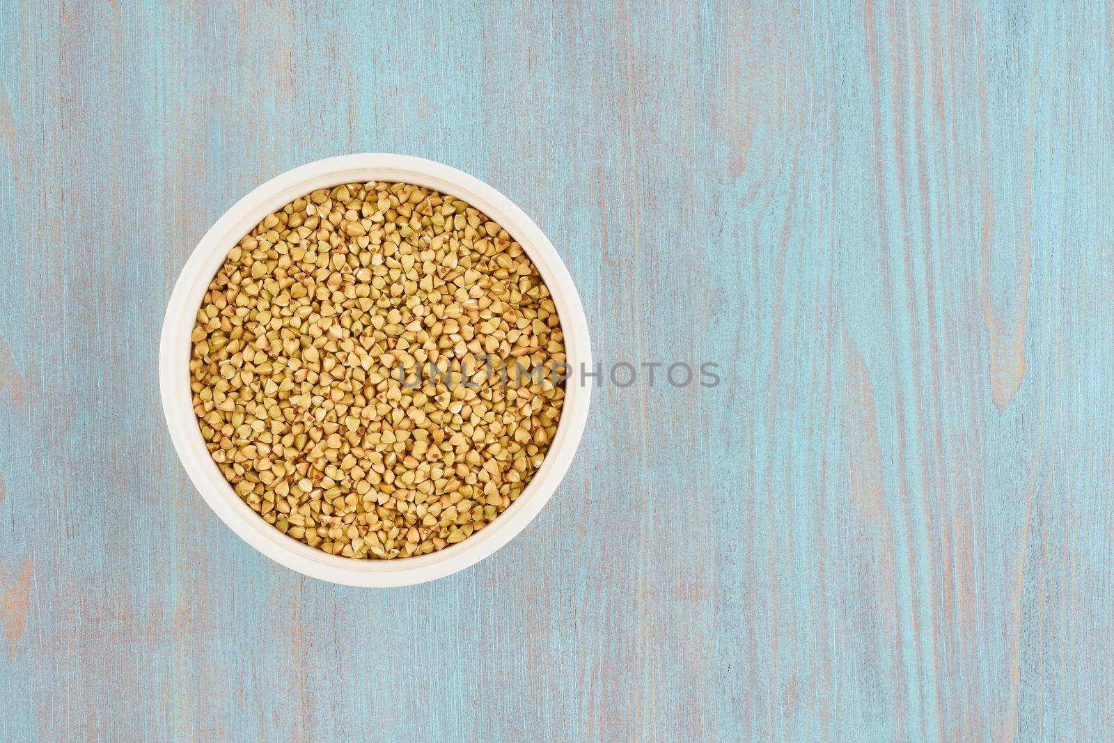 green buckwheat in white bowl on blue wooden table, gluten free wholegrain, fodmap diet, copy space