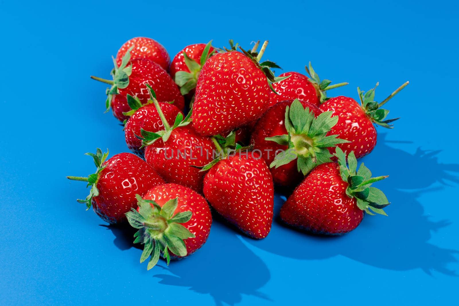 Bunch of strawberries on blue background. Red berry summer seasonal fruit