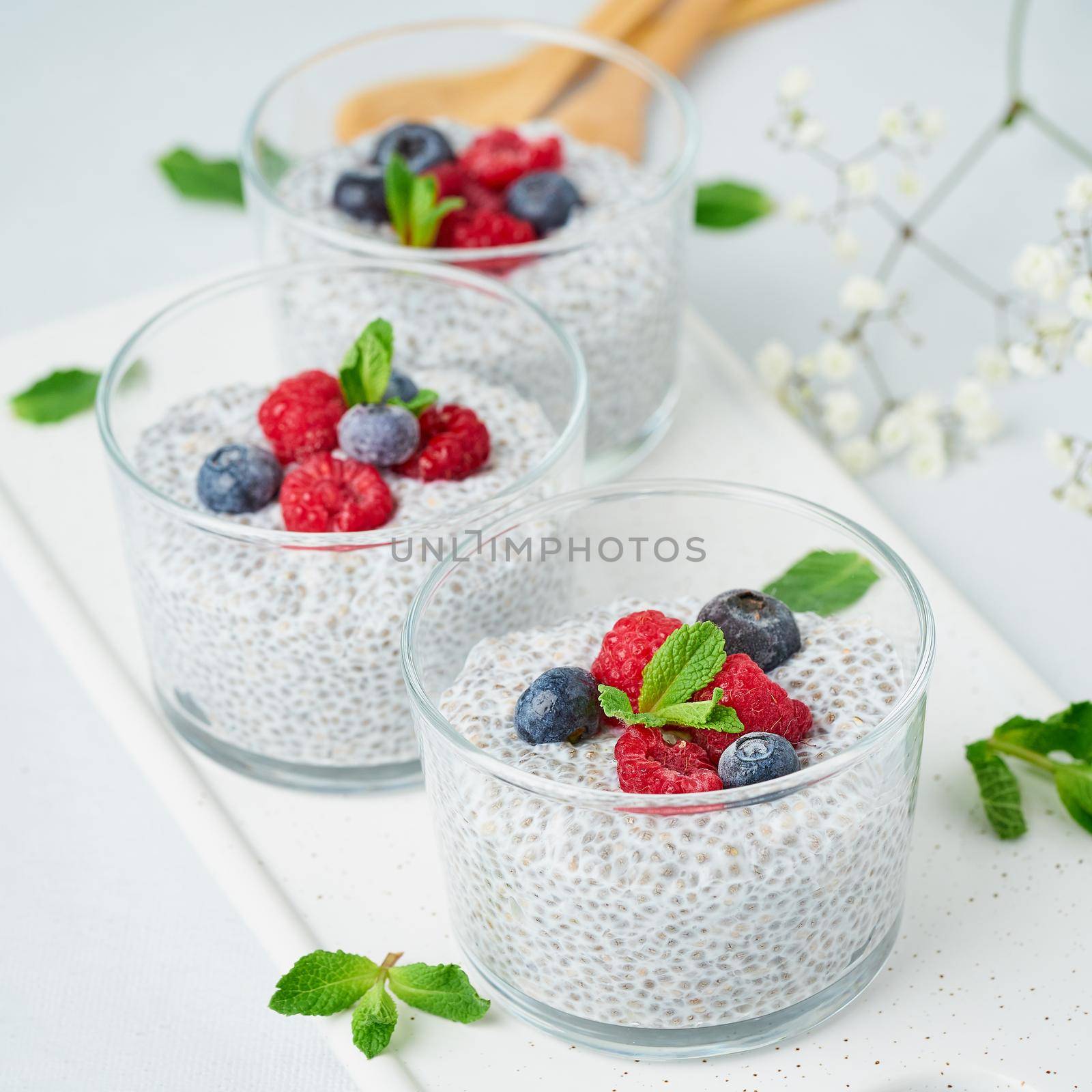Chia pudding with fresh berries raspberries, blueberries. Three glass, light background, side view, flowers, close up