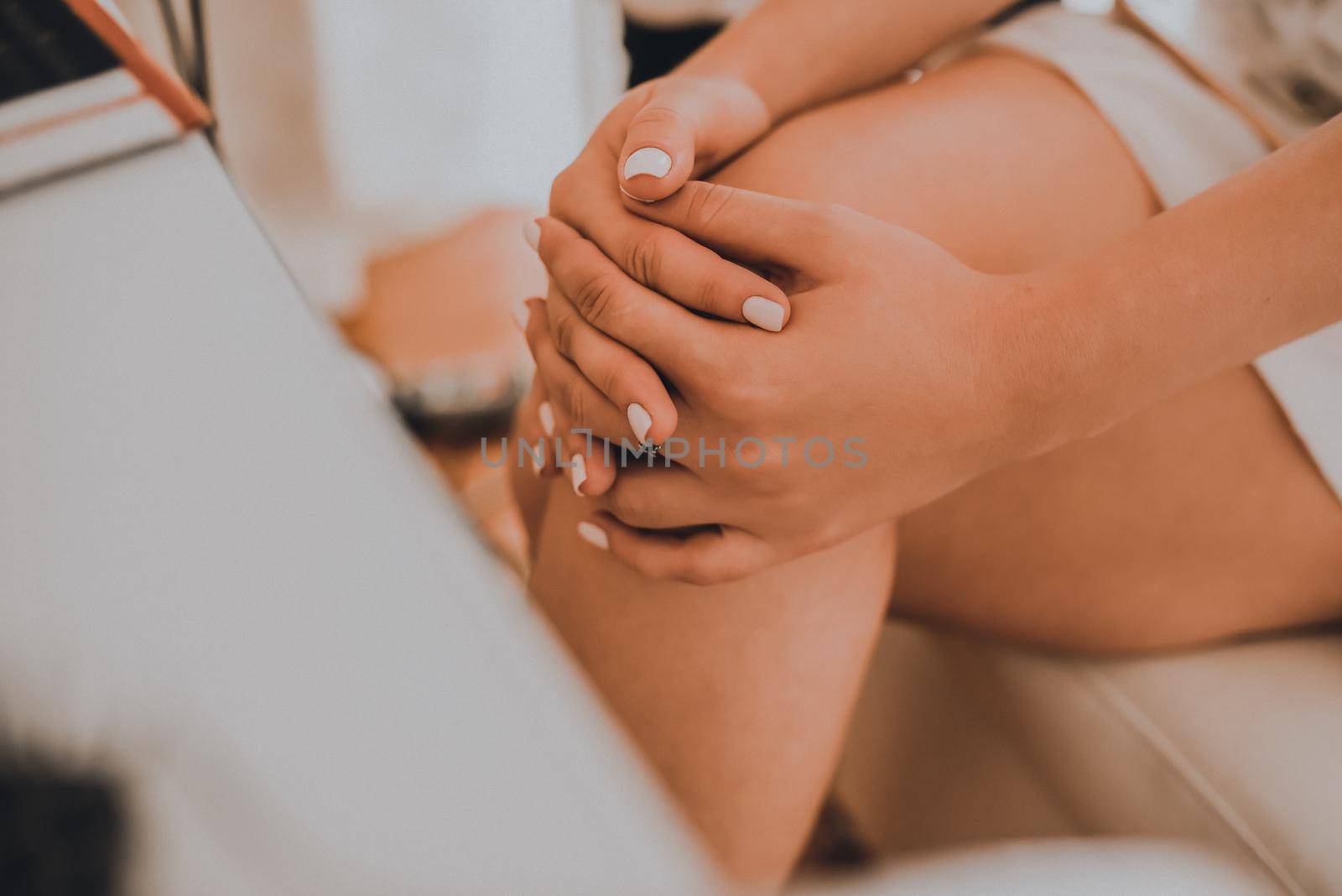 The girl sits with her legs crossed at a white cosmetic table. The bride in a white wedding dress with an open neckline. Various professional cosmetics hairbrush female accessories laid out on the tab