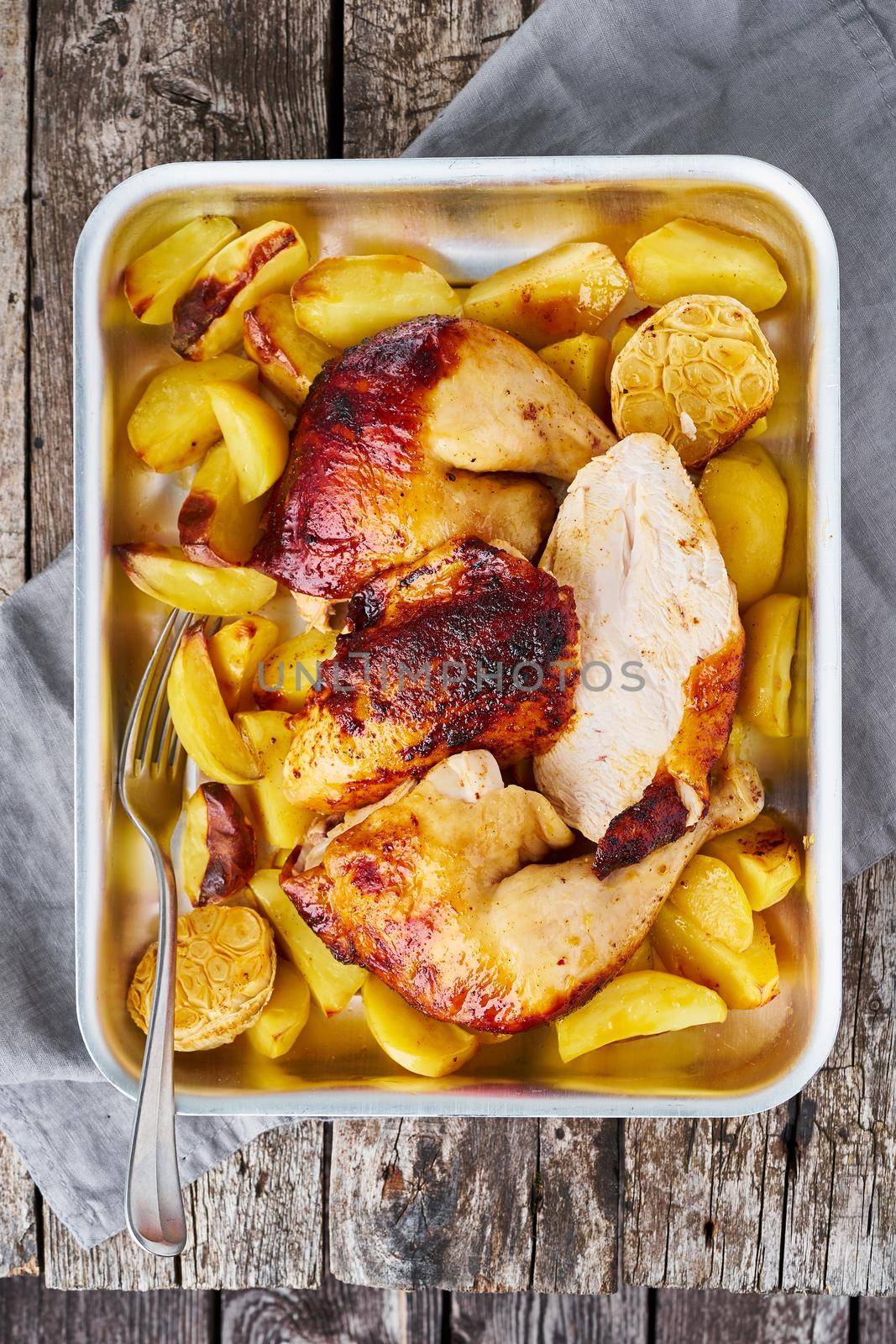 Grilled chicken meat, leg, thigh with baked potatoes, garlic. Vertical, top view. Gray old wooden table.