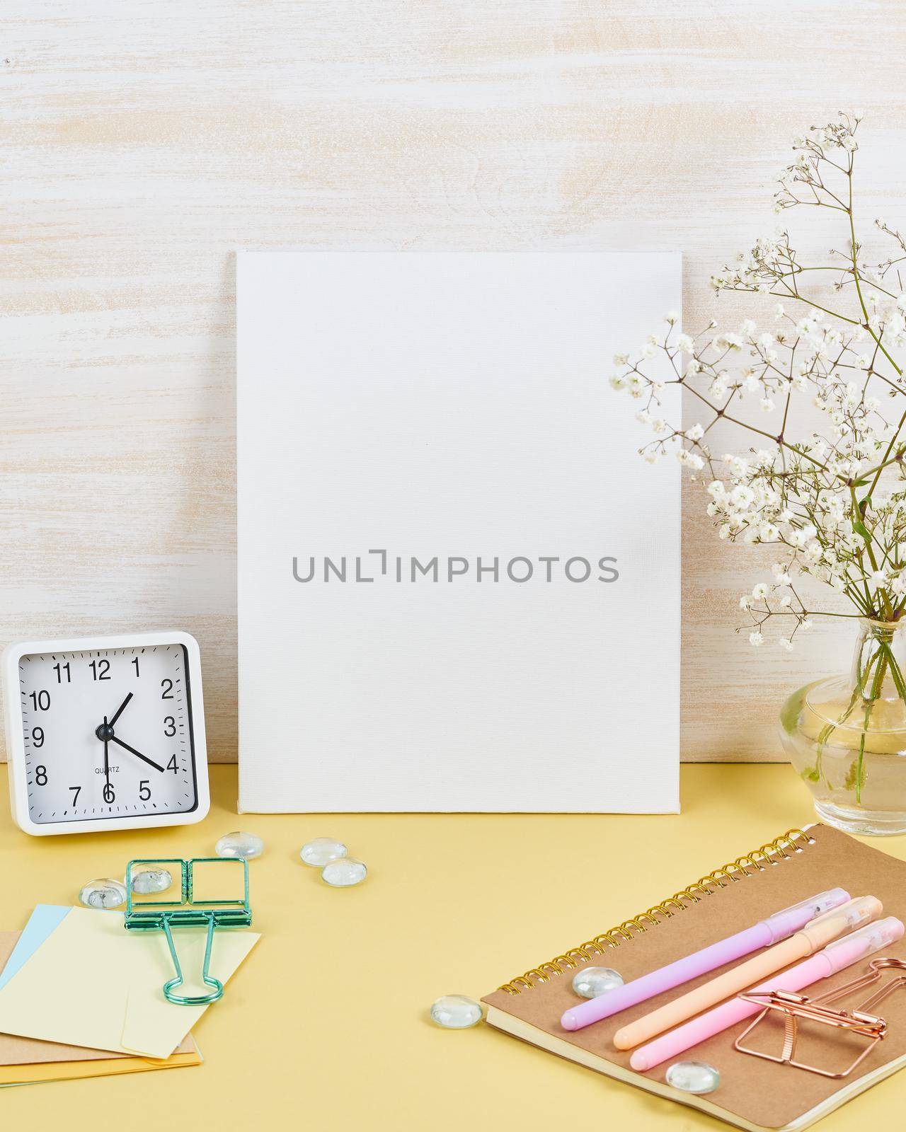 Mockup with blank white frame on yellow table against wooden wall, alarm, flower in vaze, vertical by NataBene