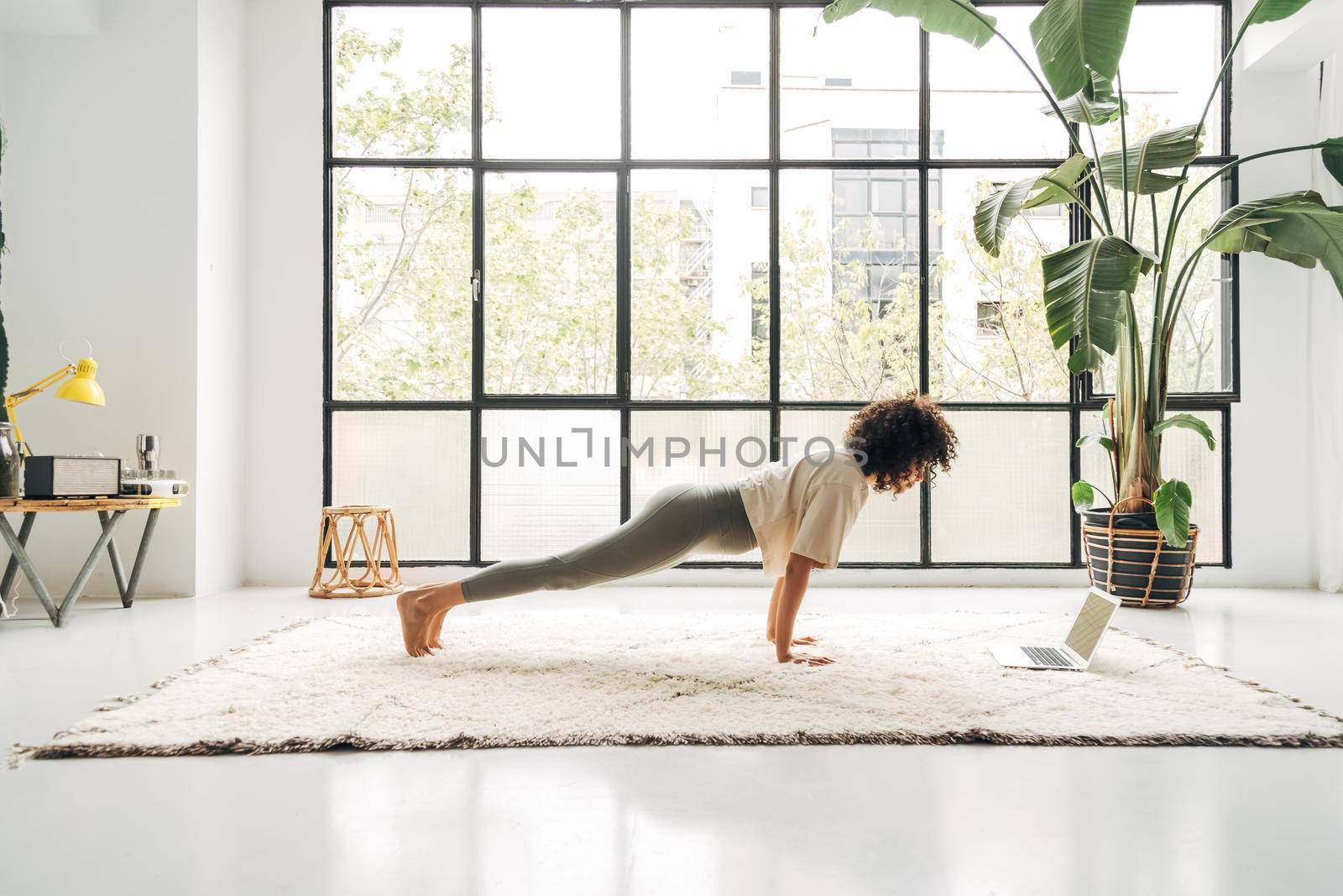Young mixed race woman exercising at home doing plank pose using online video training with laptop. Copy space. Active and healthy lifestyle concept.