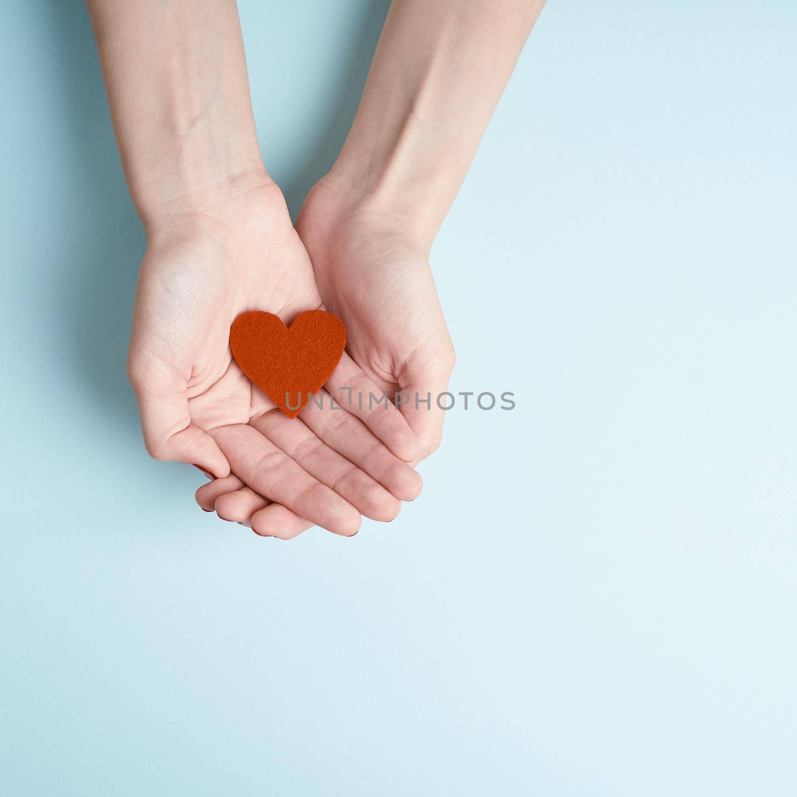 person holding red heart in hands, donate and family insurance concept, on aquamarine background by NataBene