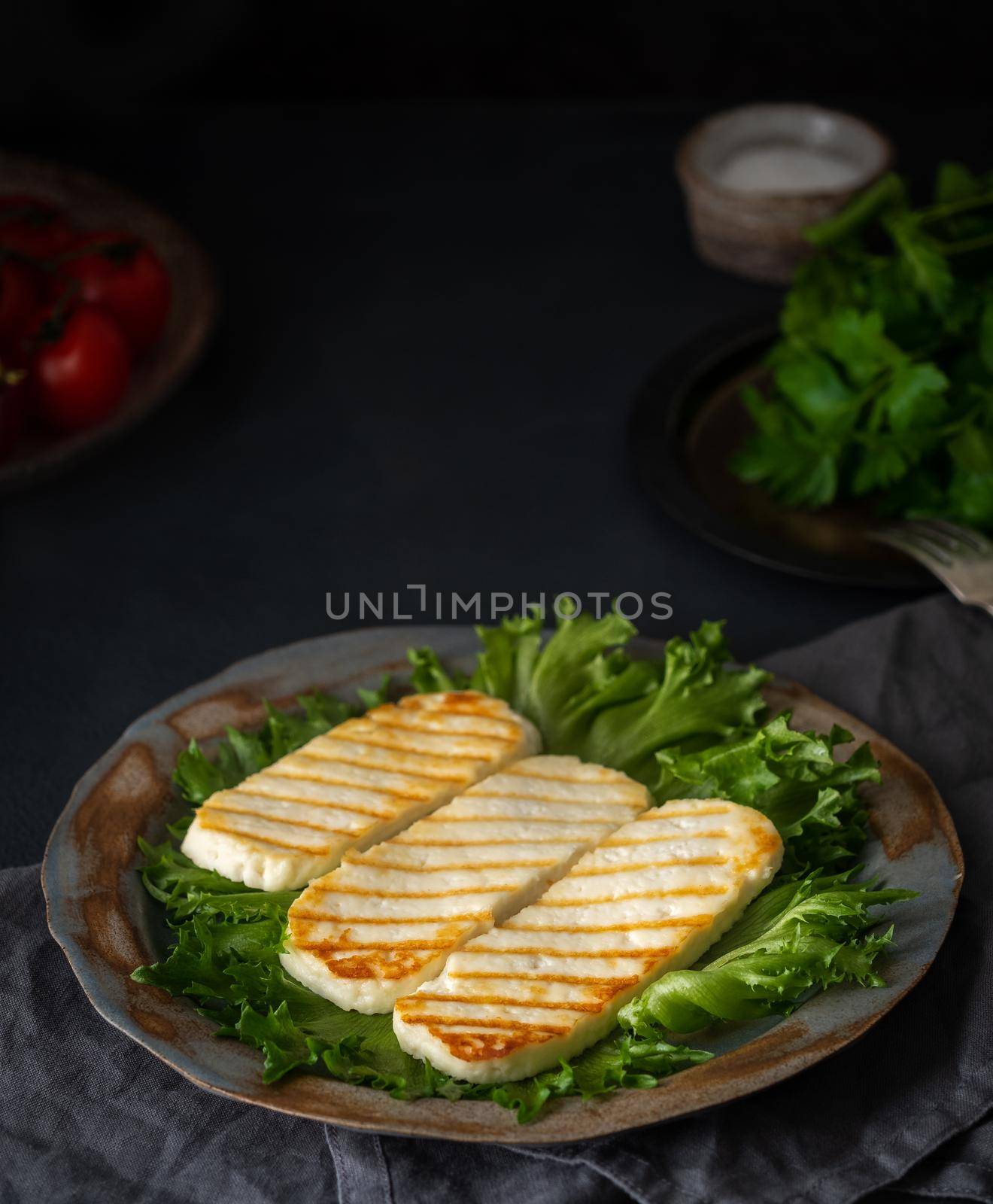 Grilled Halloumi, fried cheese with lettuce salad. Balanced diet on dark background, side view, vertical by NataBene