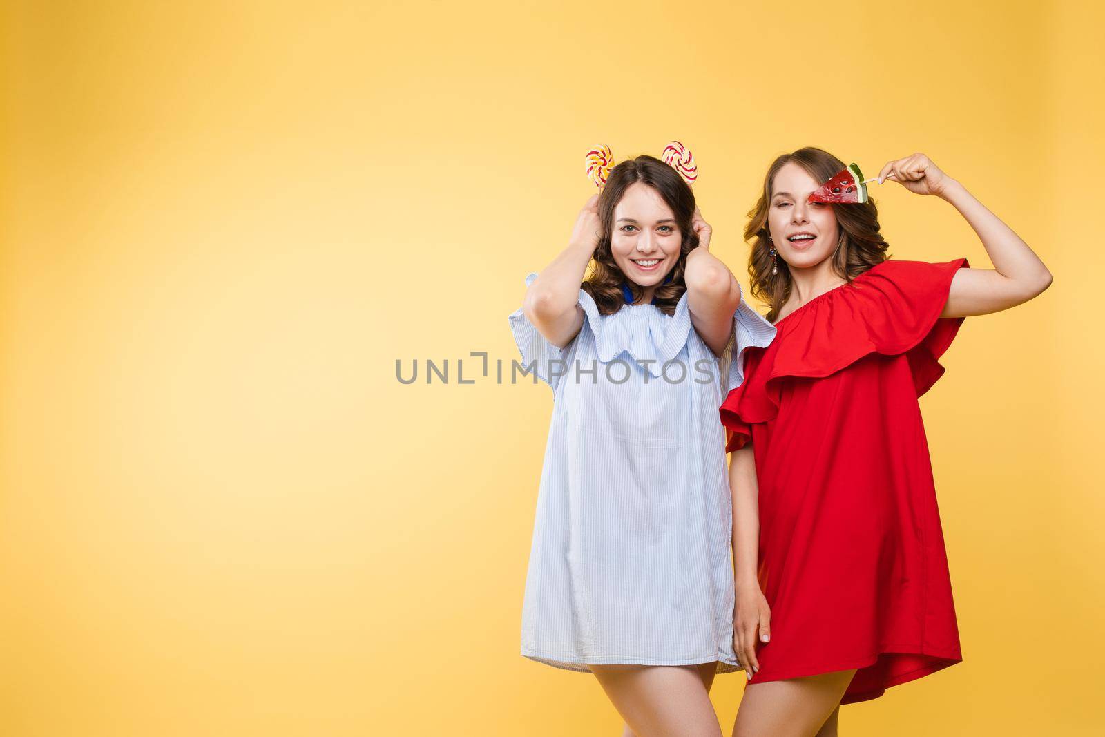 Horizontal portrait of two cheerful young women having fun together on background.