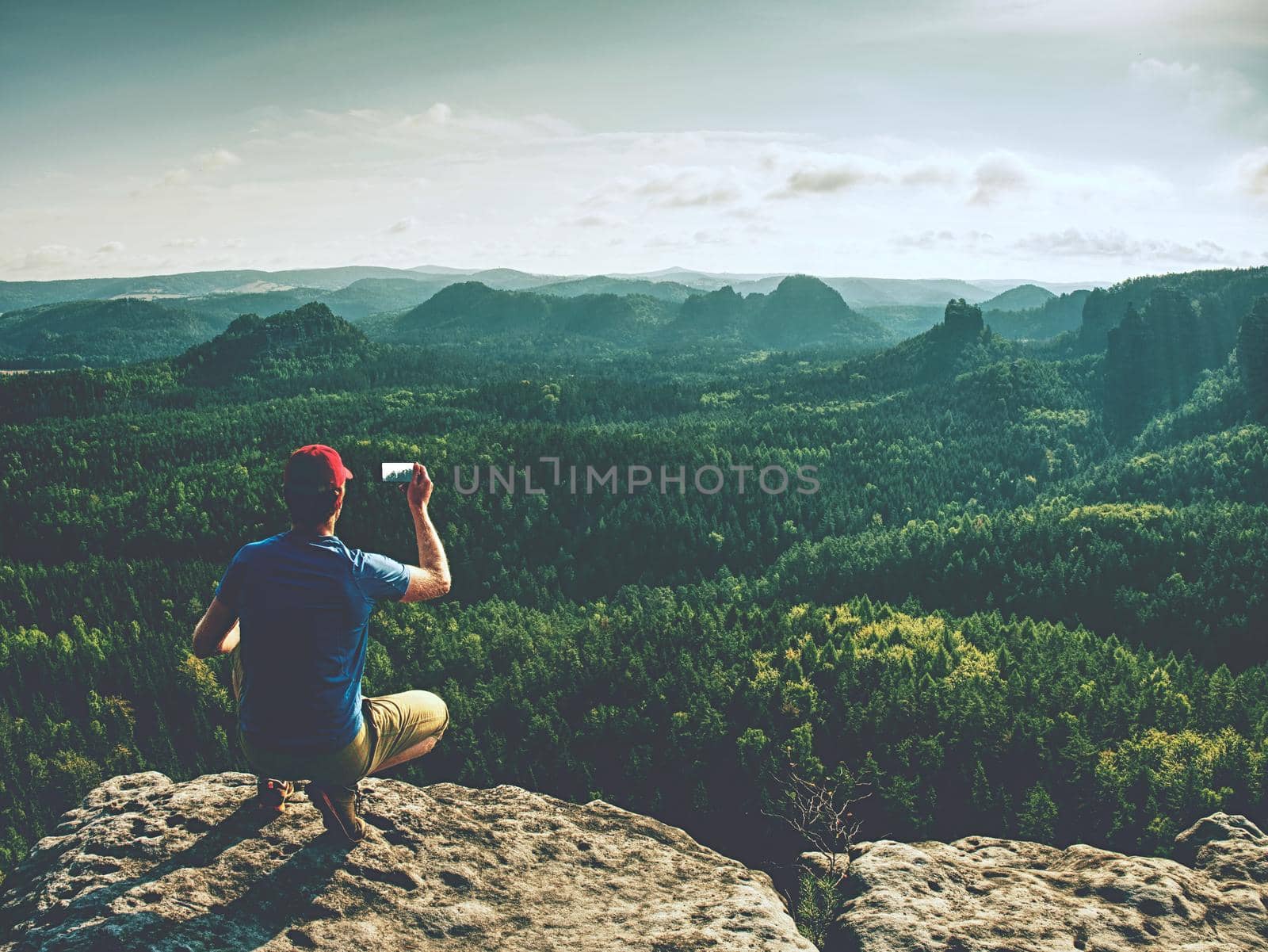 Hiking man taking panoramic picture of mountain landscape using smartphone.