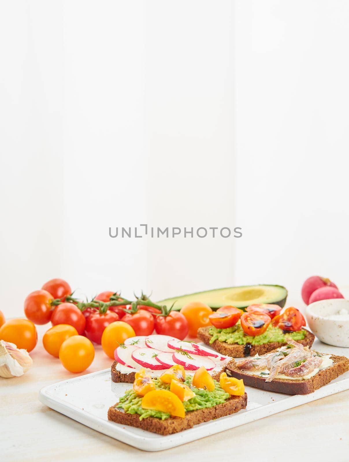 Set of smorrebrods with fish, anchovies, avocado, tomatoes, radish. Side view, copy space, white background.