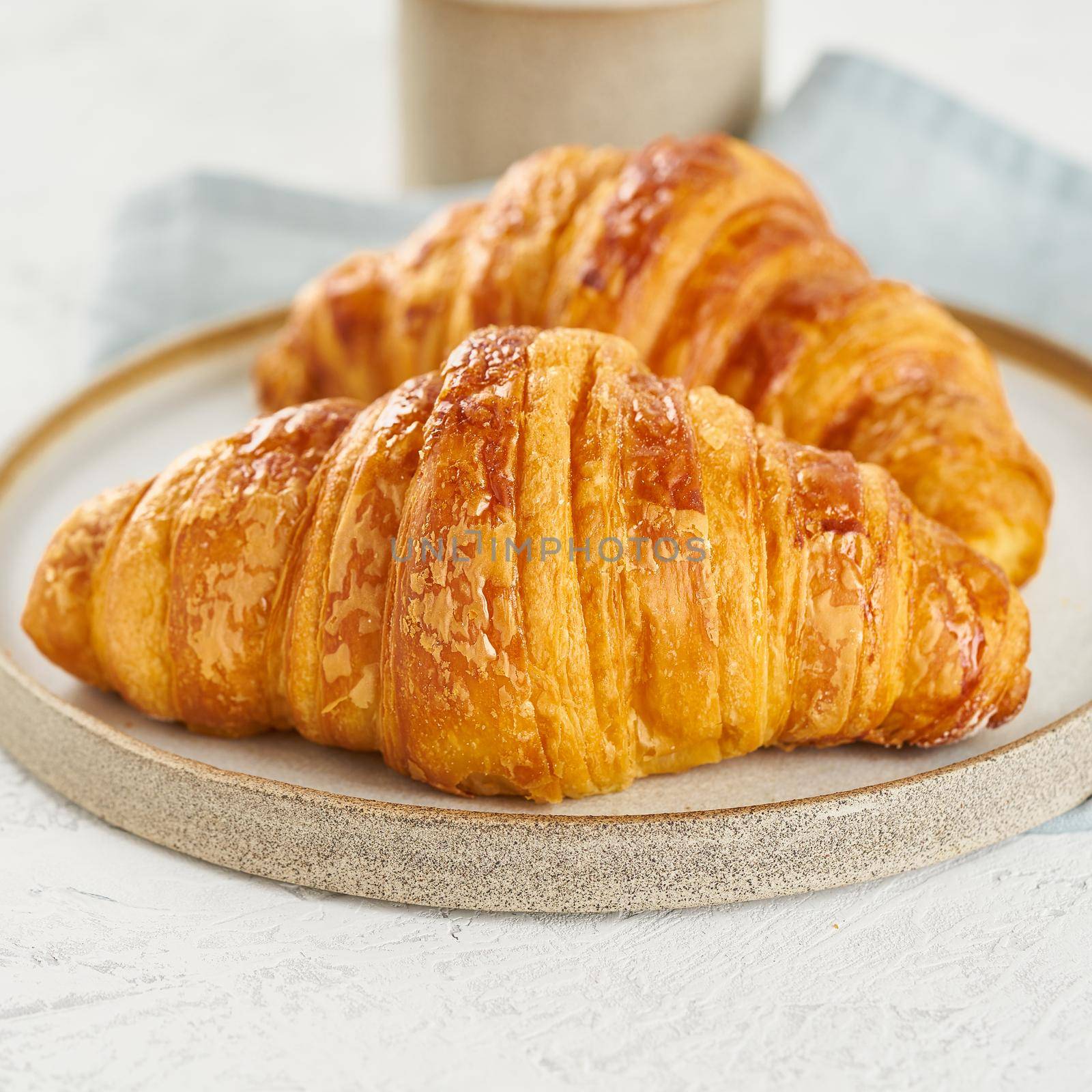 Two delicious croissants on a plate and a hot drink in a mug. Morning French breakfast with fresh pastries. Light gray background, close up, macro