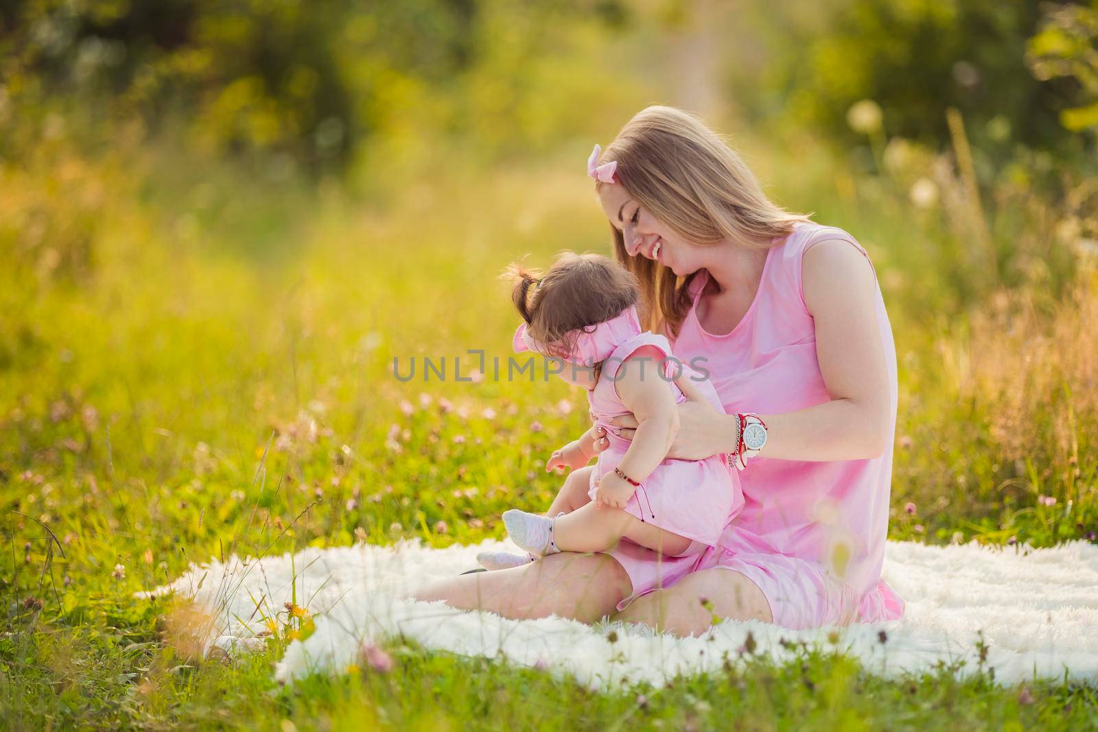 mother and daughter in identical pink dresses are sitting in nature