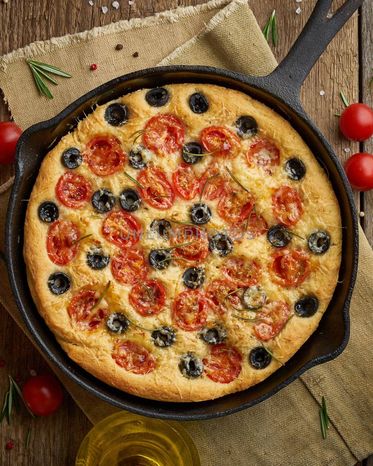 Focaccia, pizza in skillet, italian flat bread with tomatoes, olives and rosemary. Wooden table by NataBene
