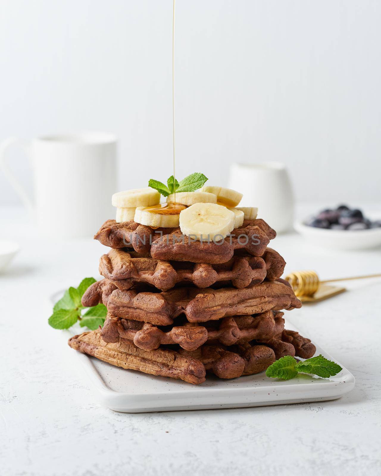 Chocolate banana waffles with maple syrup on white table, side view, vertical. Sweet brunch, a maple syrup flow.
