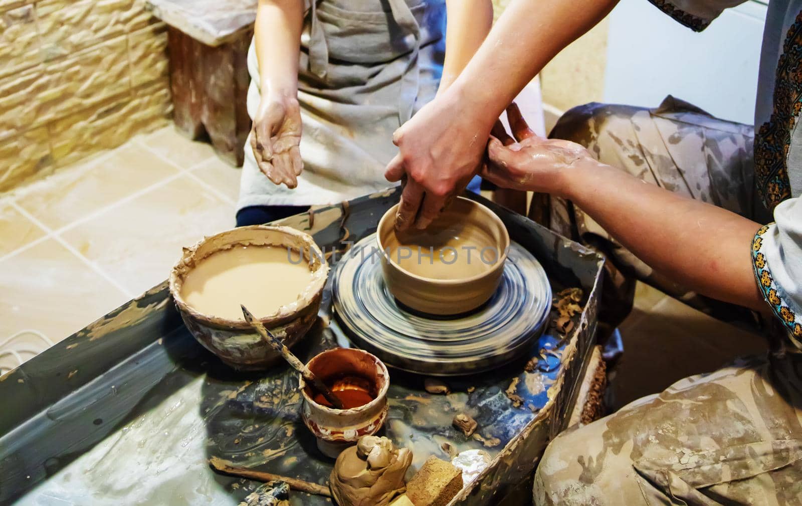 the Hands of a master and a student make a pitcher on a Potters wheel of yellow clay. Selective focus on hands
