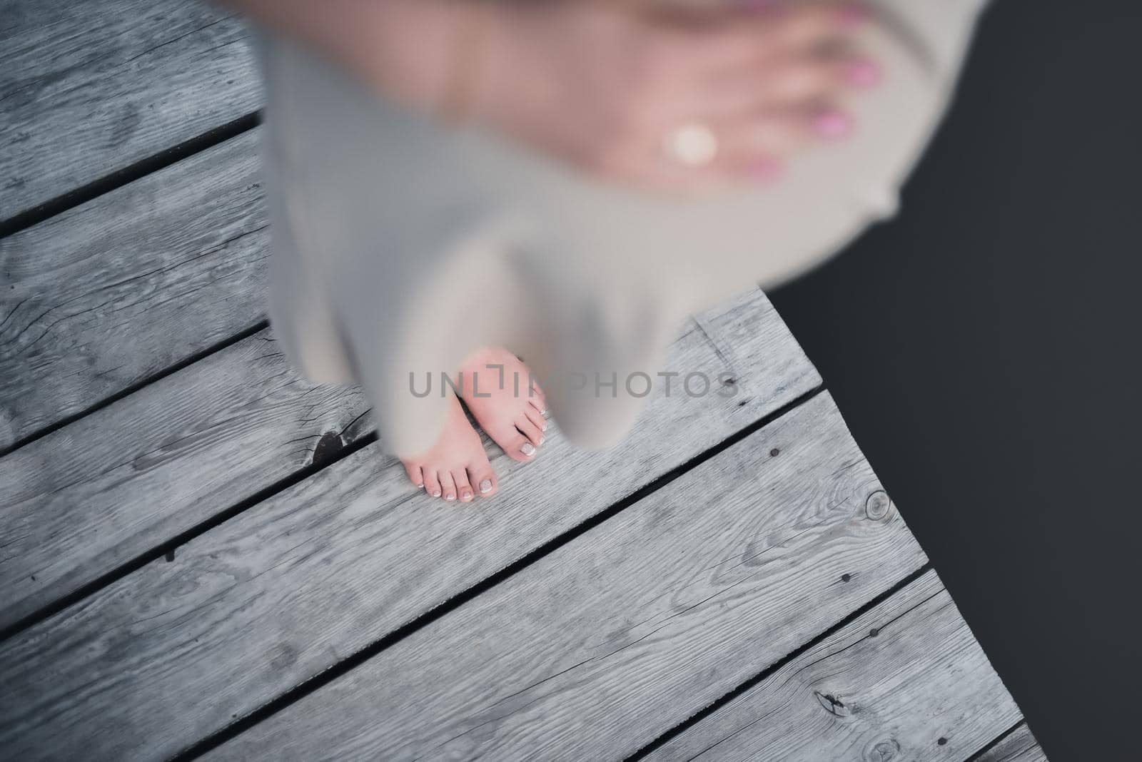 The legs of a pregnant woman in a dress are standing on a gray wooden bridge. view from above