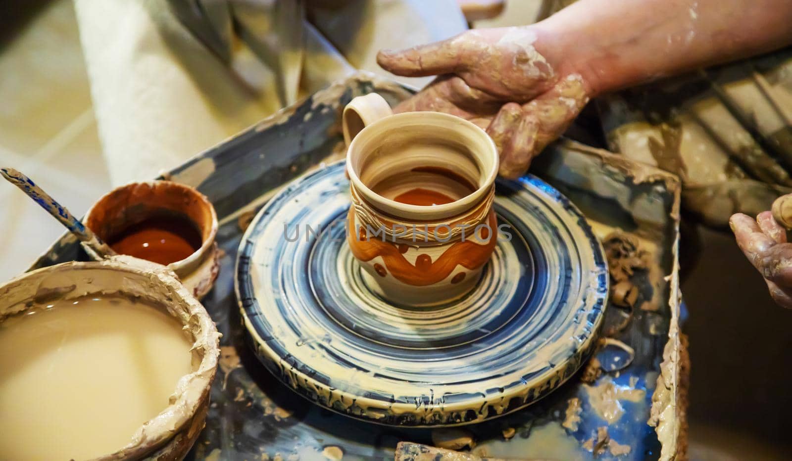 the Hands of a master and a student make a pitcher on a Potters wheel of yellow clay. Selective focus on hands