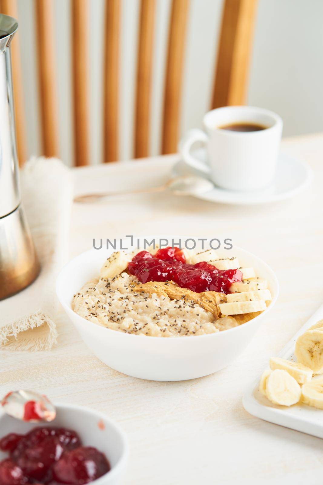 Oatmeal with strawberry jam, peanut butter, banana, Chia on white wooden light background. Vertical. Healthy vegan diet breakfast