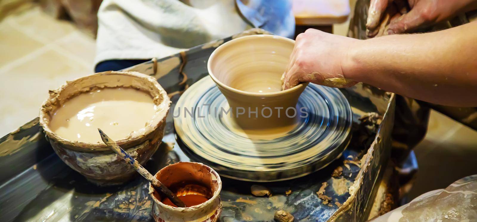 the Hands of a master and a student make a pitcher on a Potters wheel of yellow clay. Selective focus on hands by mila1784