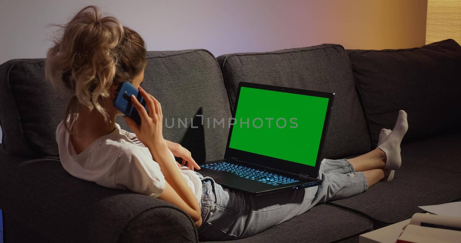 Woman sitting on couch working on laptop computer Mock up Green Screen Chroma Key dispay and talking on phone. Freelancer using pc, browsing on internet for social media advertising.