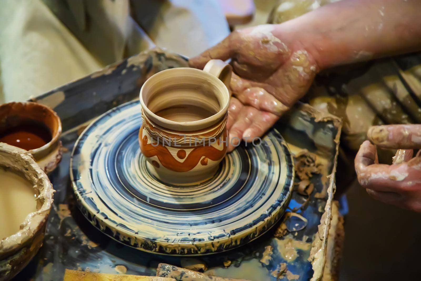 the Hands of a master and a student make a pitcher on a Potters wheel of yellow clay. Selective focus on hands