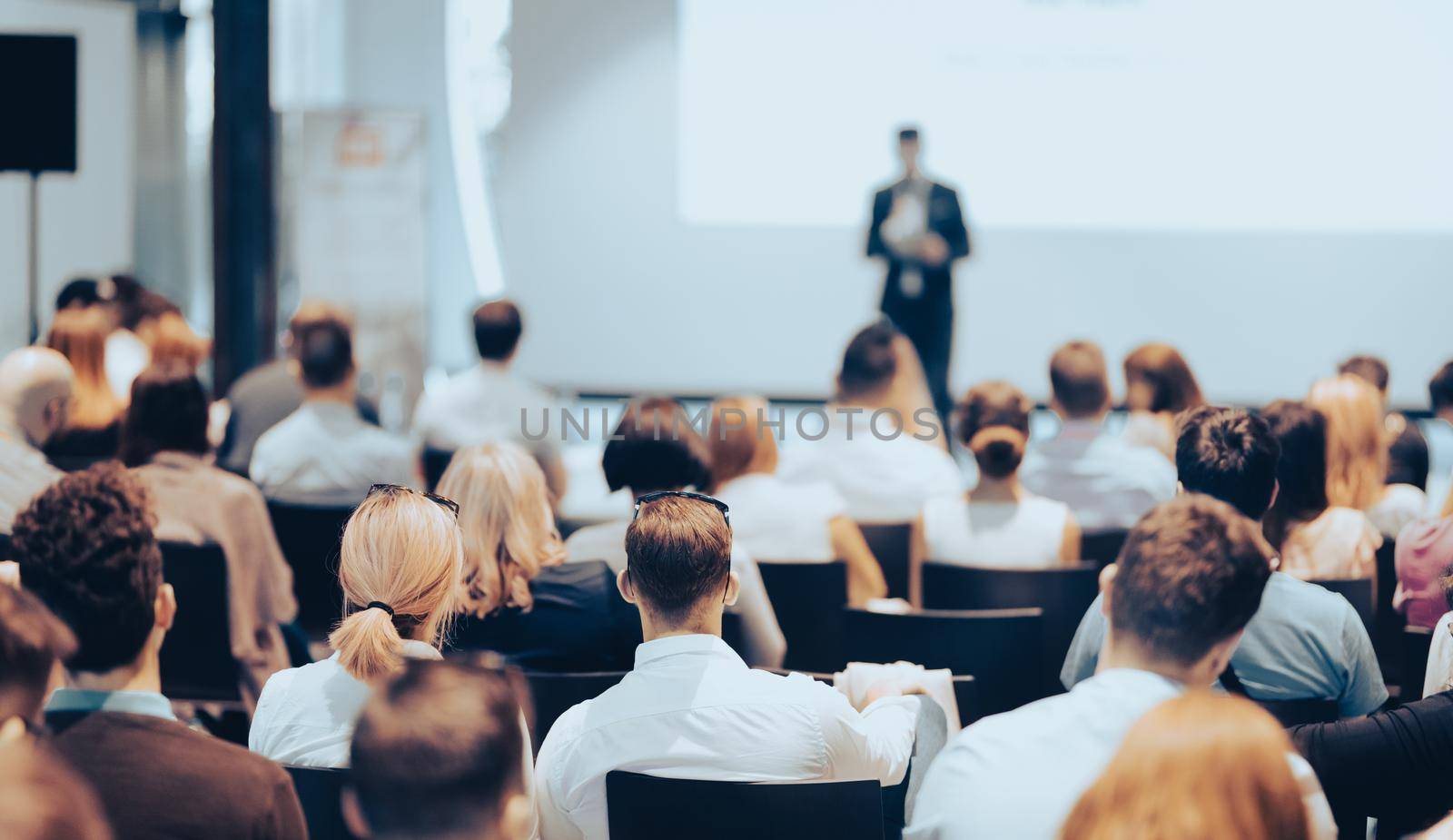 Speaker giving a talk in conference hall at business event. Rear view of unrecognizable people in audience at the conference hall. Business and entrepreneurship concept.