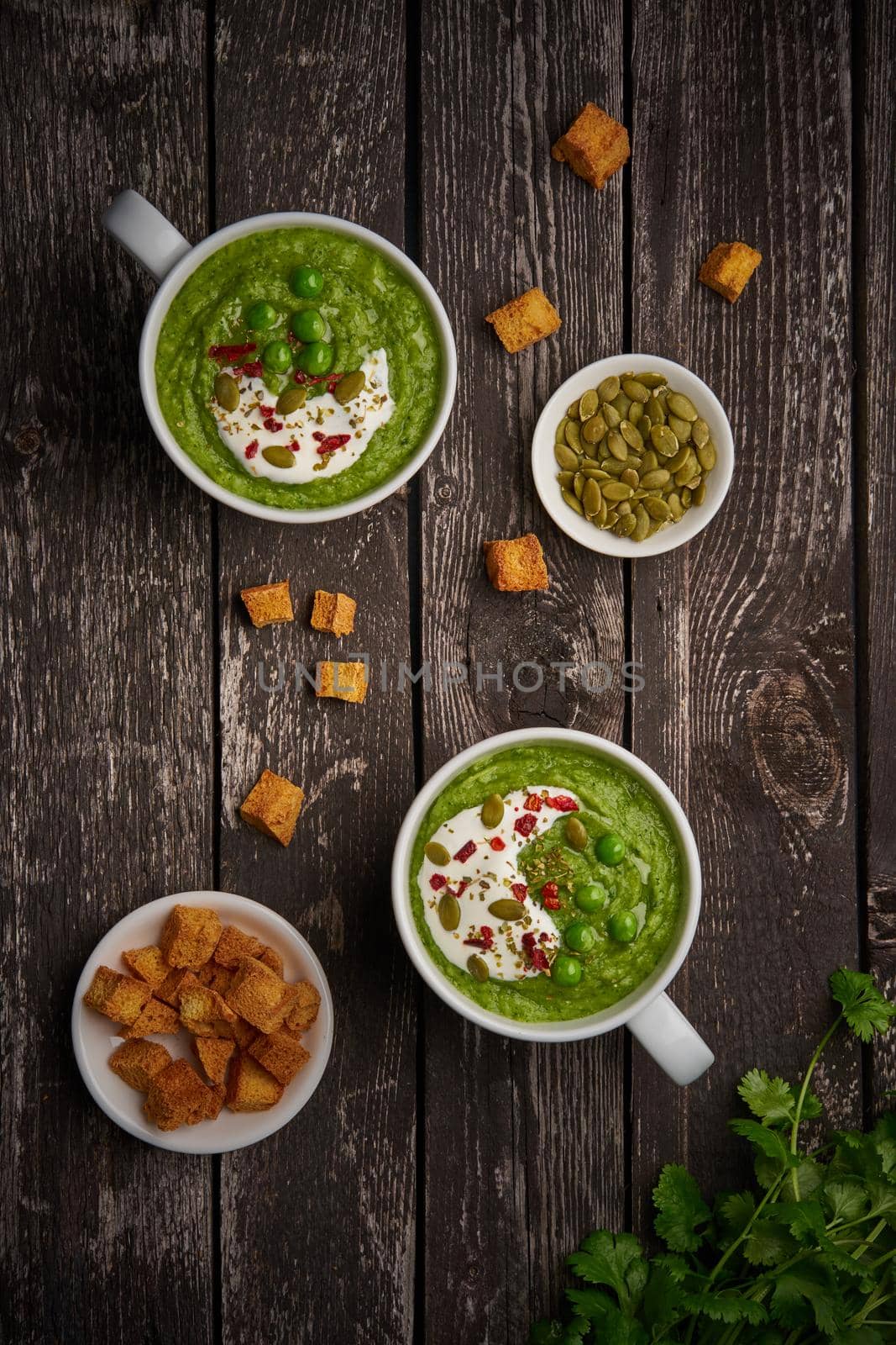 Broccoli cream soup, vertical, copy space, top view. Vegetable green puree in two large white cup. Diet vegan soup of broccoli, zucchini, green peas on dark wooden background by NataBene