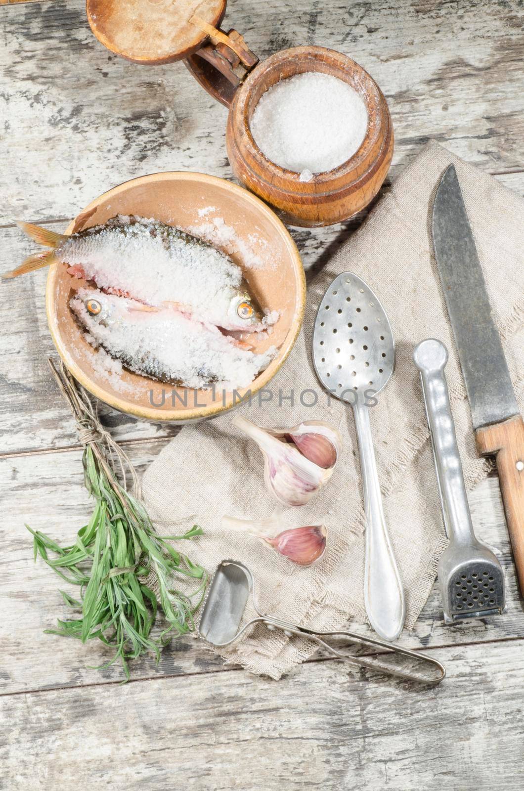 Two roaches fish in ceramic bowl with salt, near the old cutlery. From the series "Still Life with fresh fish"