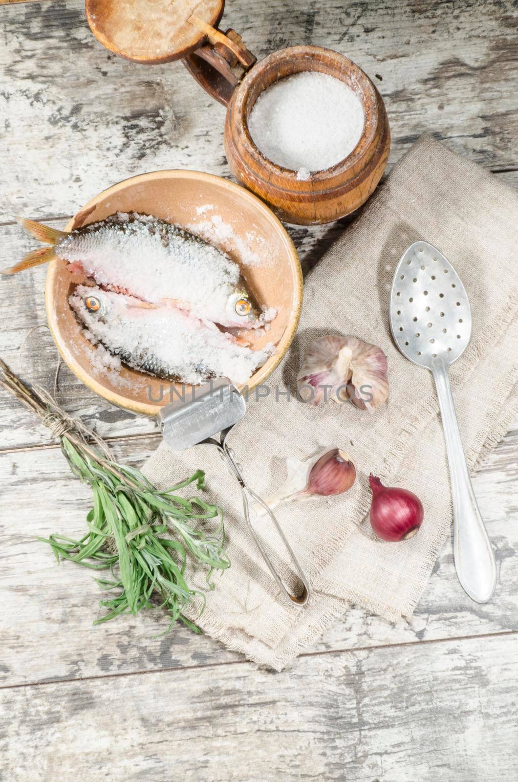 Two roaches fish in ceramic bowl with salt, near the old cutlery. From the series "Still Life with fresh fish"