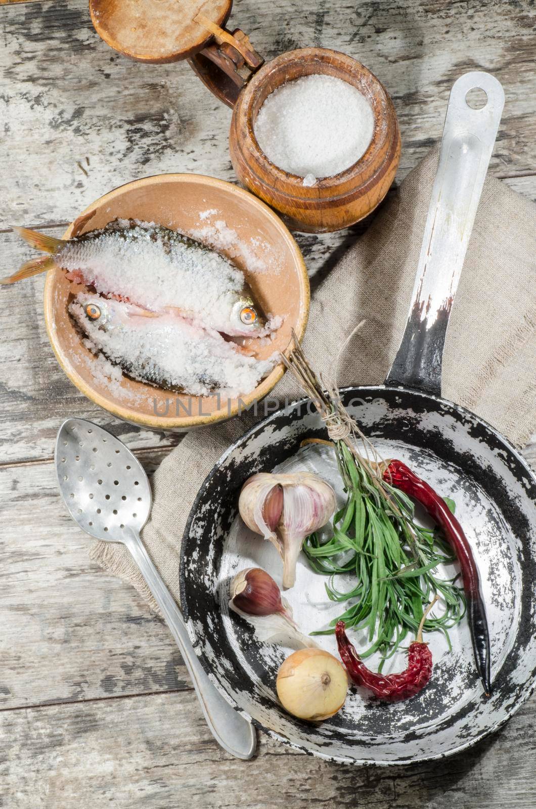 Two roaches fish in ceramic bowl with salt, near the old cutlery. From the series "Still Life with fresh fish"