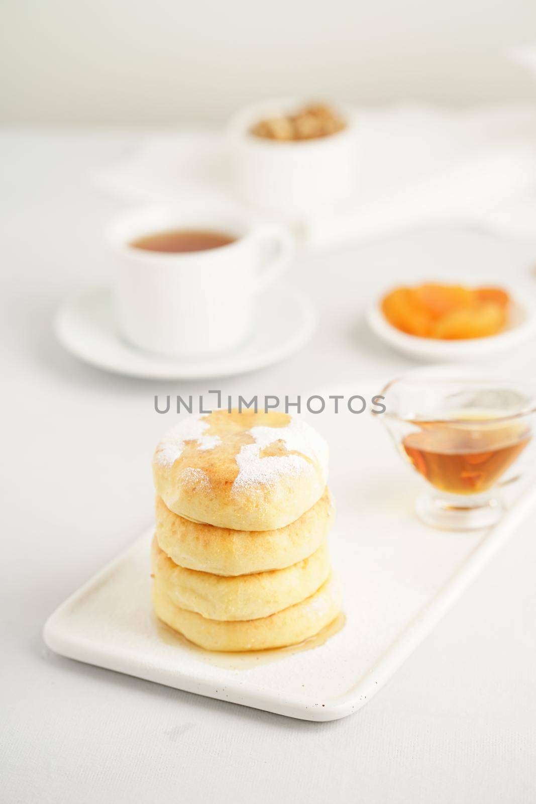 Fried cheese cakes, sweet cheese pancakes on white plate on white background, vertical. Home tea party