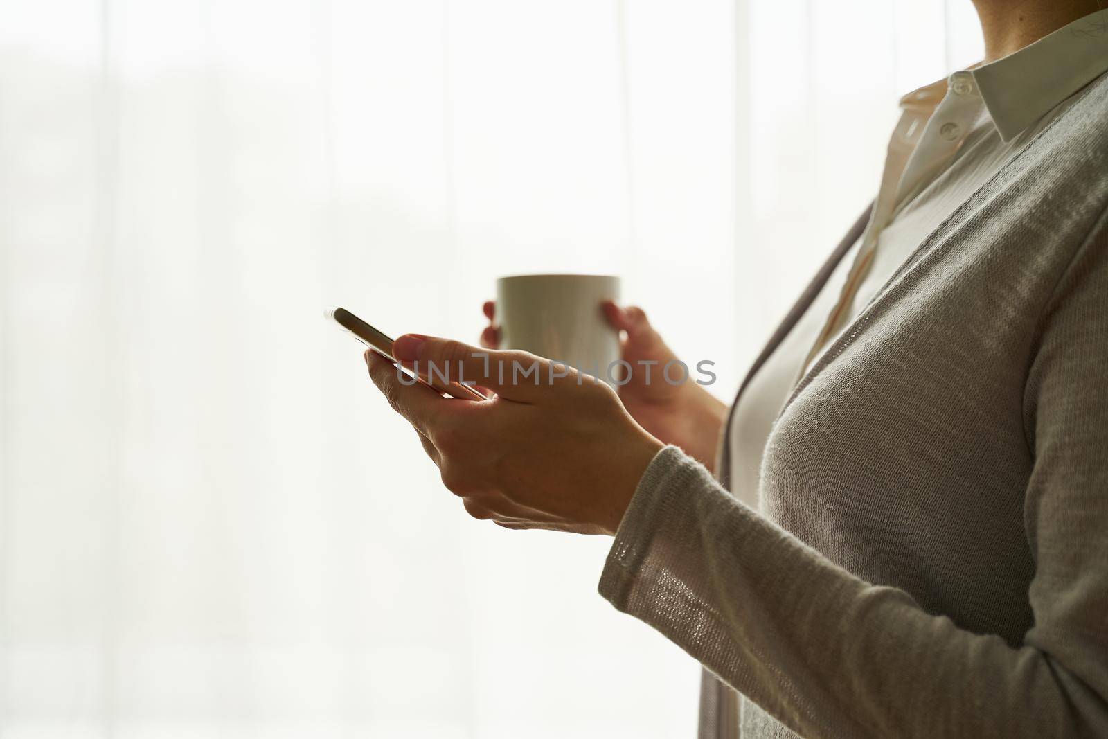 woman holding smartphone and drinking coffee/tea