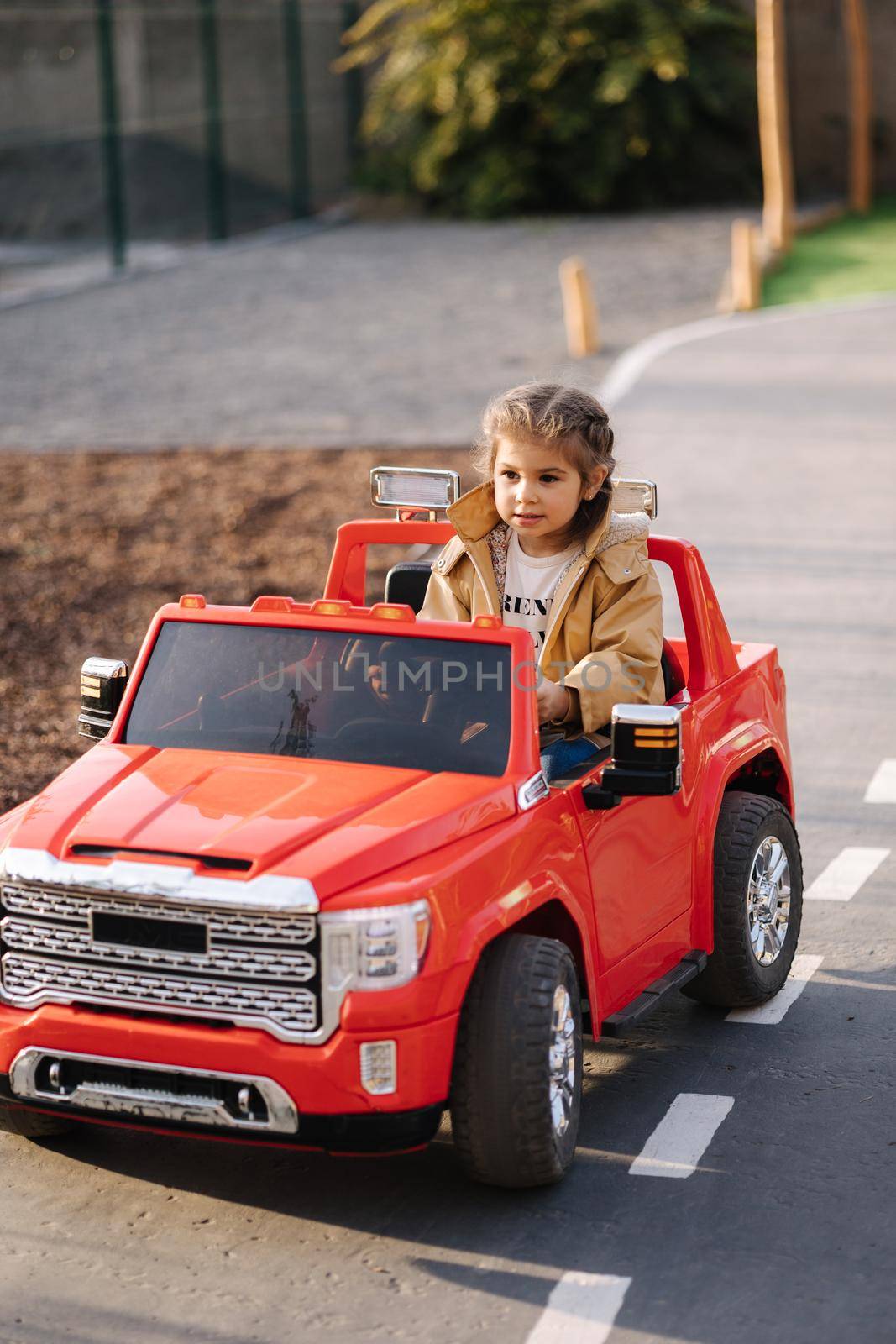 Cute little girl rides in a mini city on a red electric car jeep. Adorable little girl road in toy city. Plays for entertaiment.