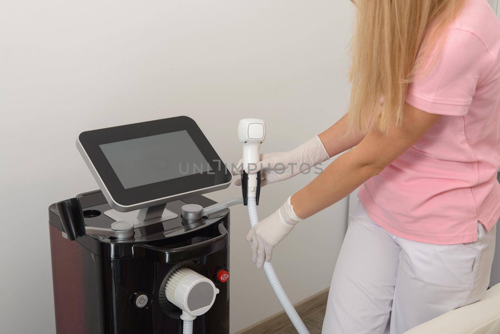 The concept of health and beauty. A young nurse in a pink t-shirt with a device for laser hair removal. by Ashtray25