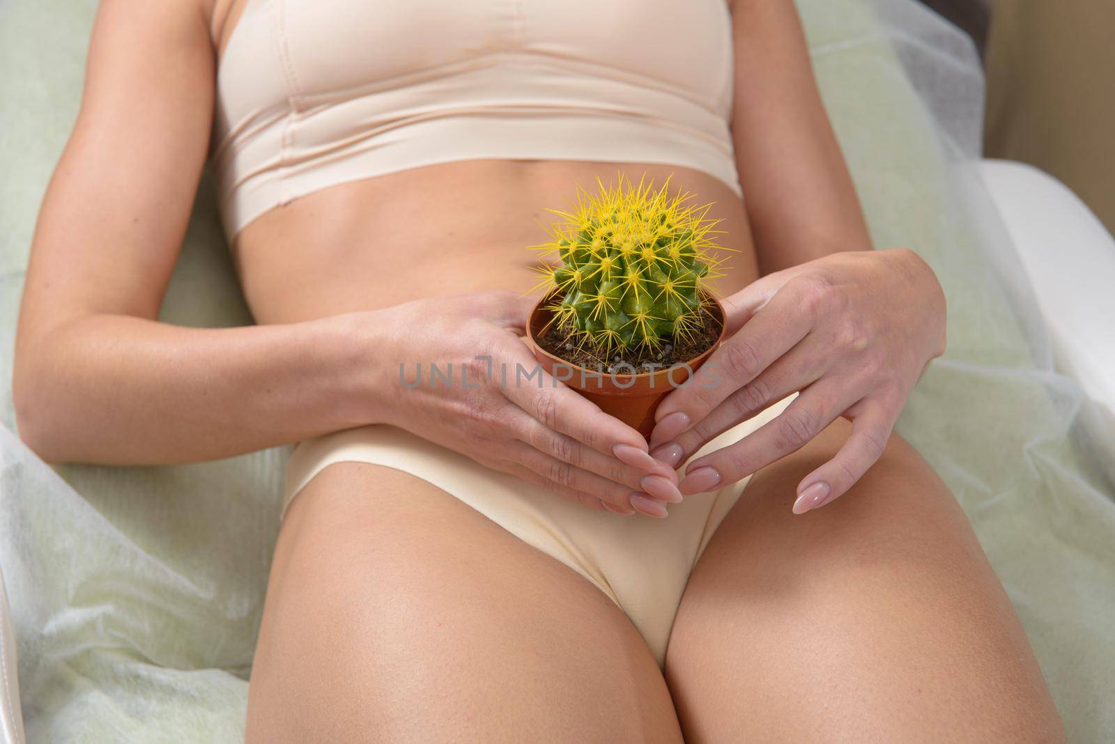 Depilation in the bikini zone concept. A woman holding a yellow cactus in her hand laying in light beige pants by Ashtray25