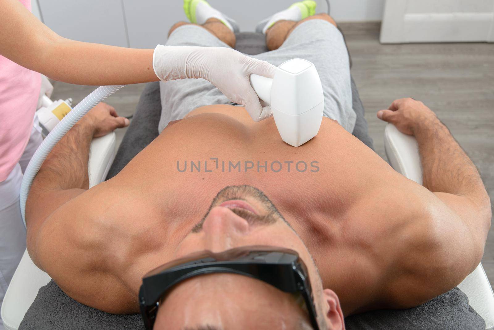 Laser hair removal on mans chest. man in a goggles. therapist in a pink t-shirt