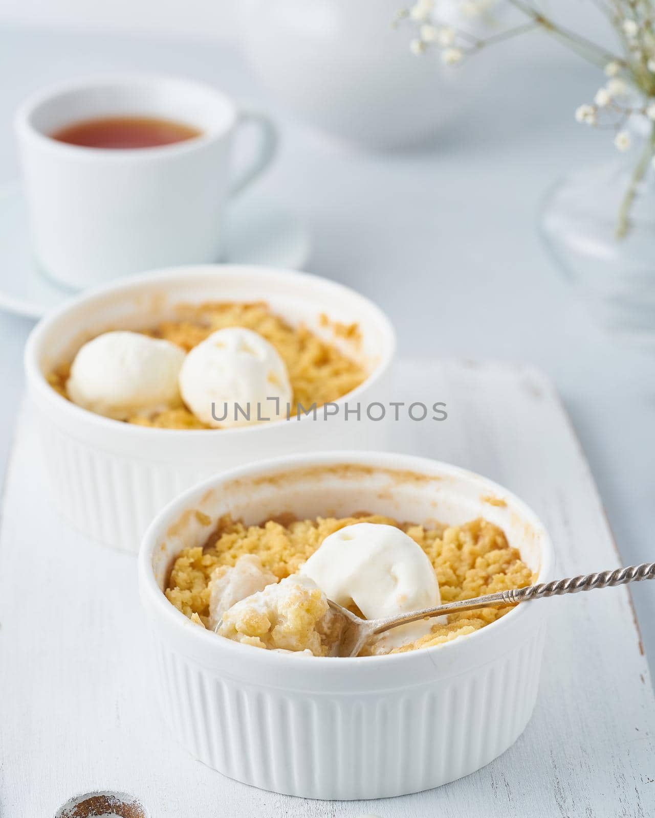 Apple crumble with ice cream, spoon with streusel. Side view, vertical. Morning breakfast on light gray table.