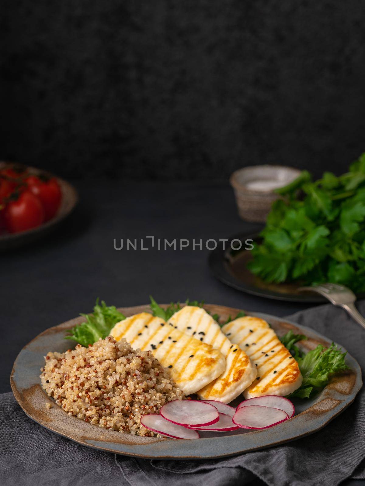 Halloumi, grilled cheese with quinoa, salad, radish. Balanced diet on dark background, side view, vertical, copy space
