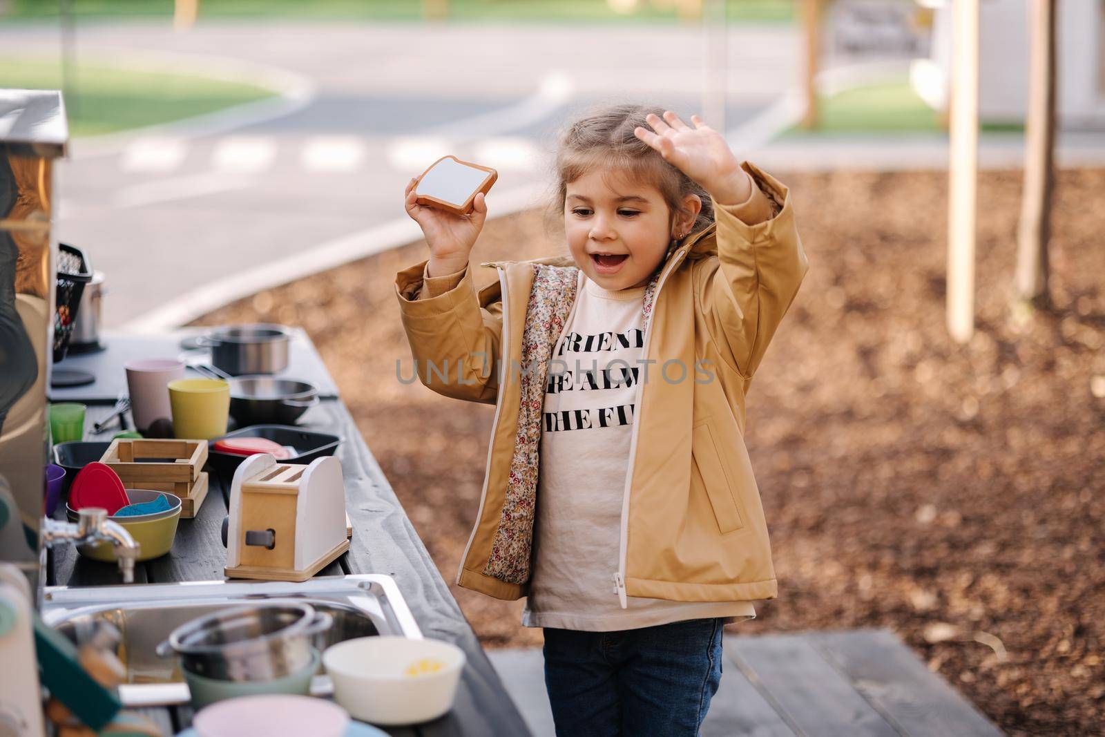 Adorable little girl playing in toy kitchen outdoors. Cute three year old girl have fun in kids city.