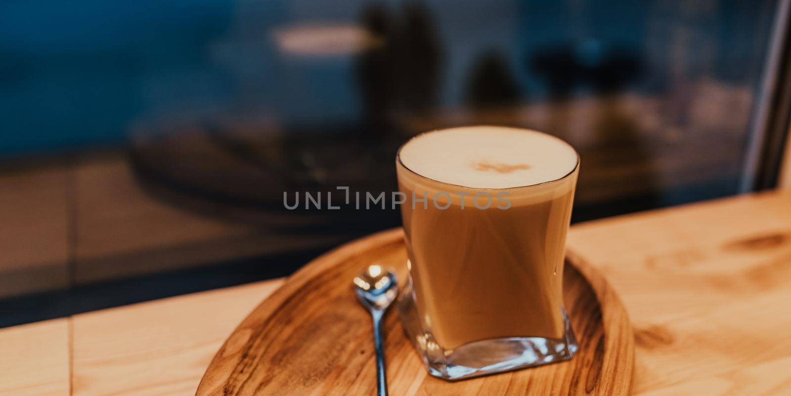 coffee latte with foam and milk in a transparent glass stands on a wooden tray with a spoon on the table