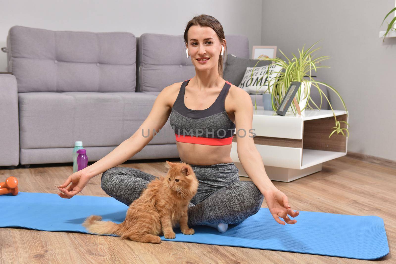 Beautiful young woman in yoga posing with red cat indoor in flat.