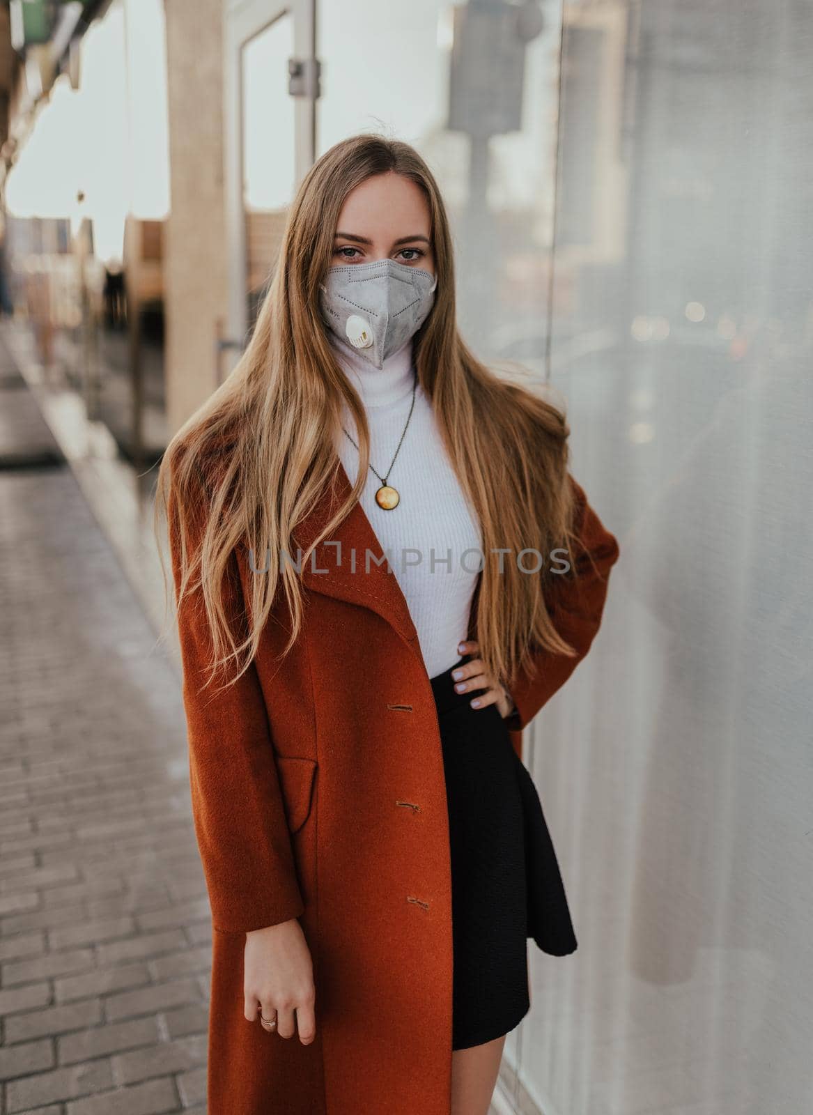 young ukrainian blonde woman in protective medical mask kn95 respirator on street against background of shop windows. coronavirus infection. accessory covid-19