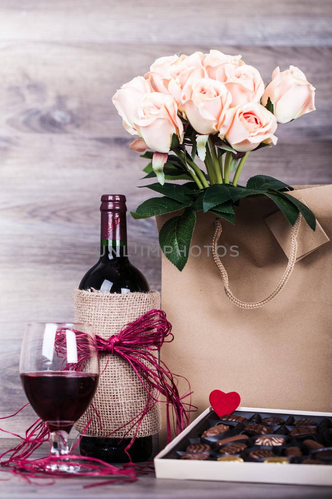 Red wine bottle, glass of wine, box of chocolates, rose with decoration by red heart on wooden table. Valentines day celebration concept. Copy space.
