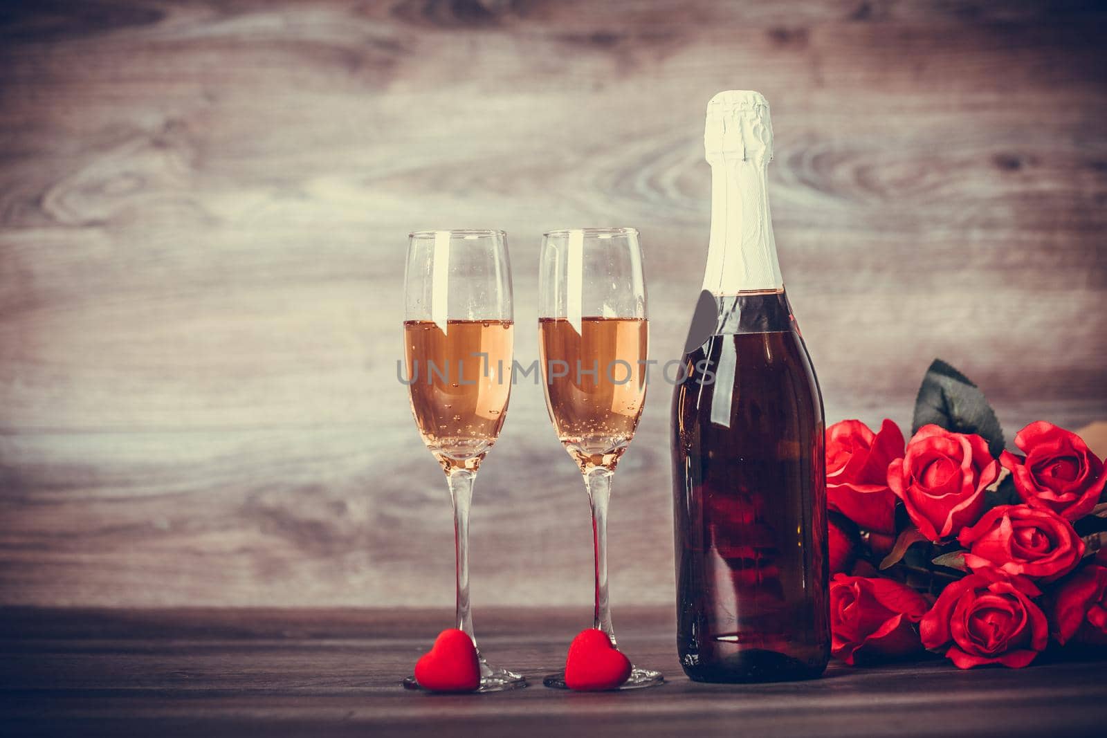 Valentines Day. Champagne, wine glasses and red roses with decoration by red heart on wooden table. Appointment, Birthday. Concept: happiness, holiday