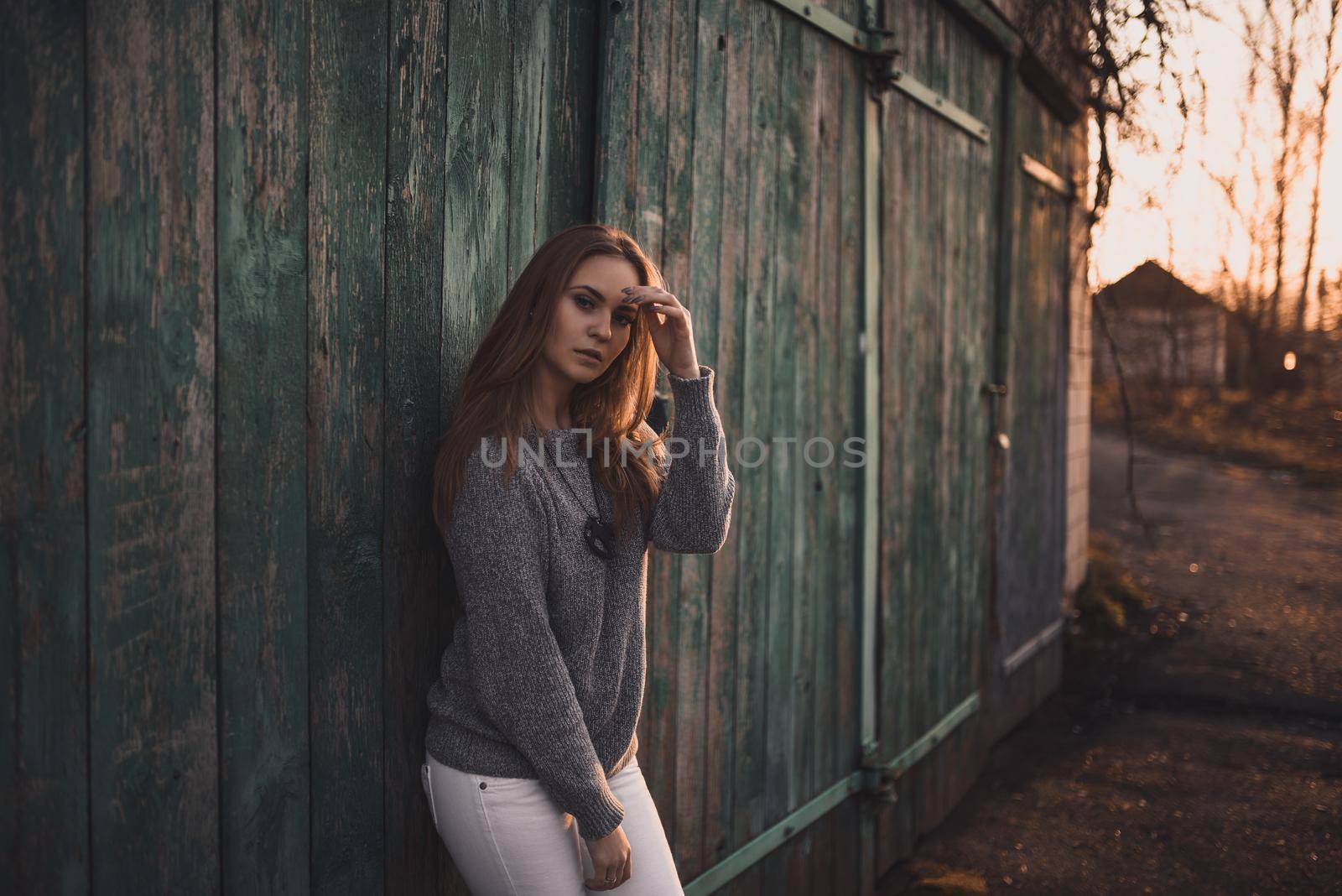 beautiful young blonde model girl. White pants. gray knitted sweater. black boots. wooden pendant on the neck in the form of a horse. On the Sunset. Portrait.