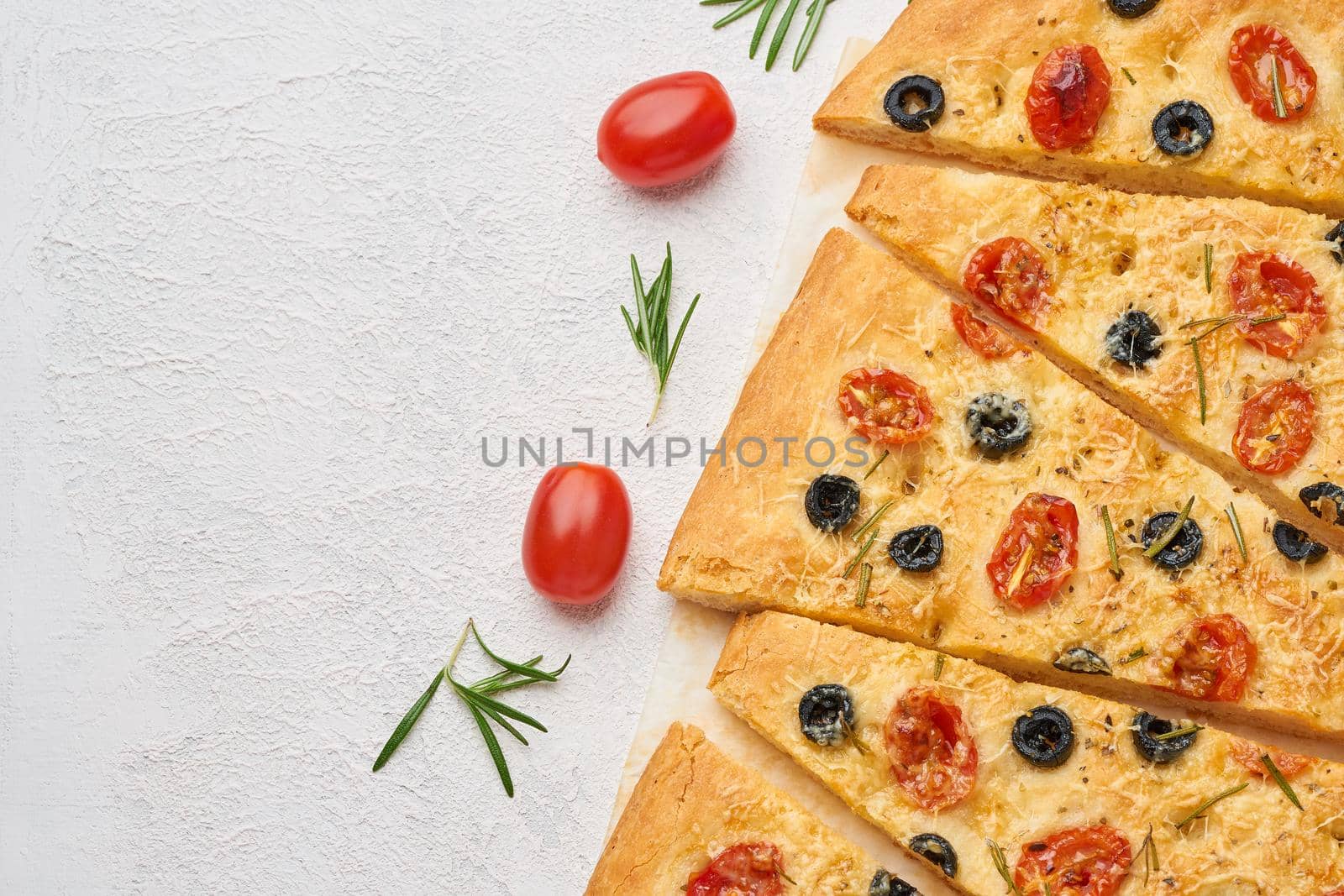 Focaccia, pizza with tomatoes, olives and a rosemary. Sliced Italian flat bread. Top view, copy space, white concrete background