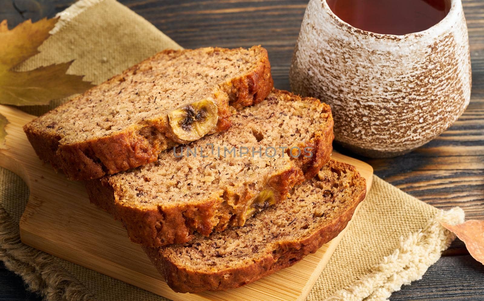 Autumn food-slices of banana bread, a Cup of tea, dry leaves, a dark wooden table. Side view, close up