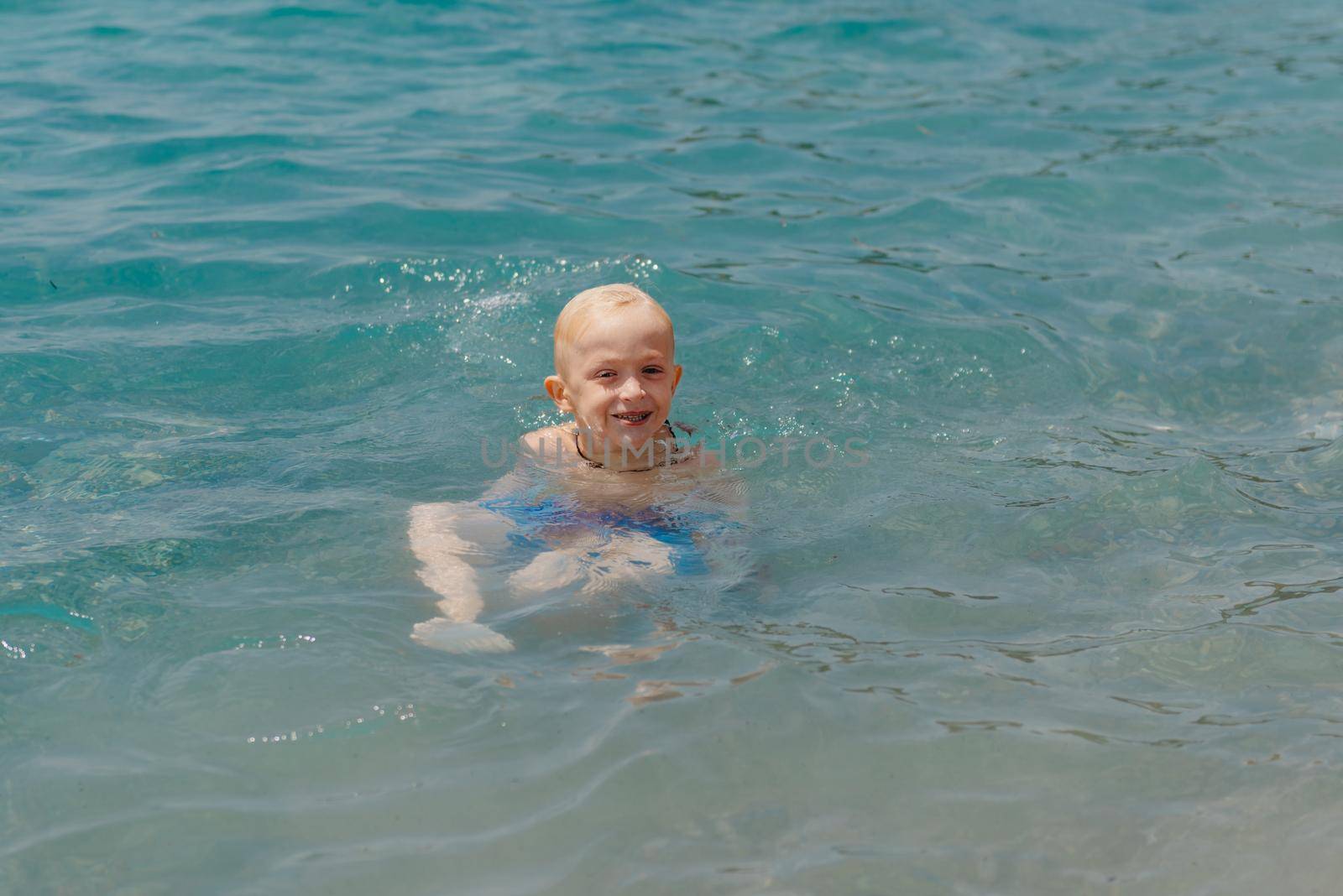 Child learning to swim in the open sea of tropical resort. Kids learn swimming. Exercise and training for young children. Little boy with colorful float board in sport club. Swimming baby or toddler. Happy child boy swims in sea in swimming circle with splash. Blue sky and water. Swimming training. Fun joy activities on vacation in the beach. Childhood moments lifestyle. Freedom careless. boy swim in the sea.