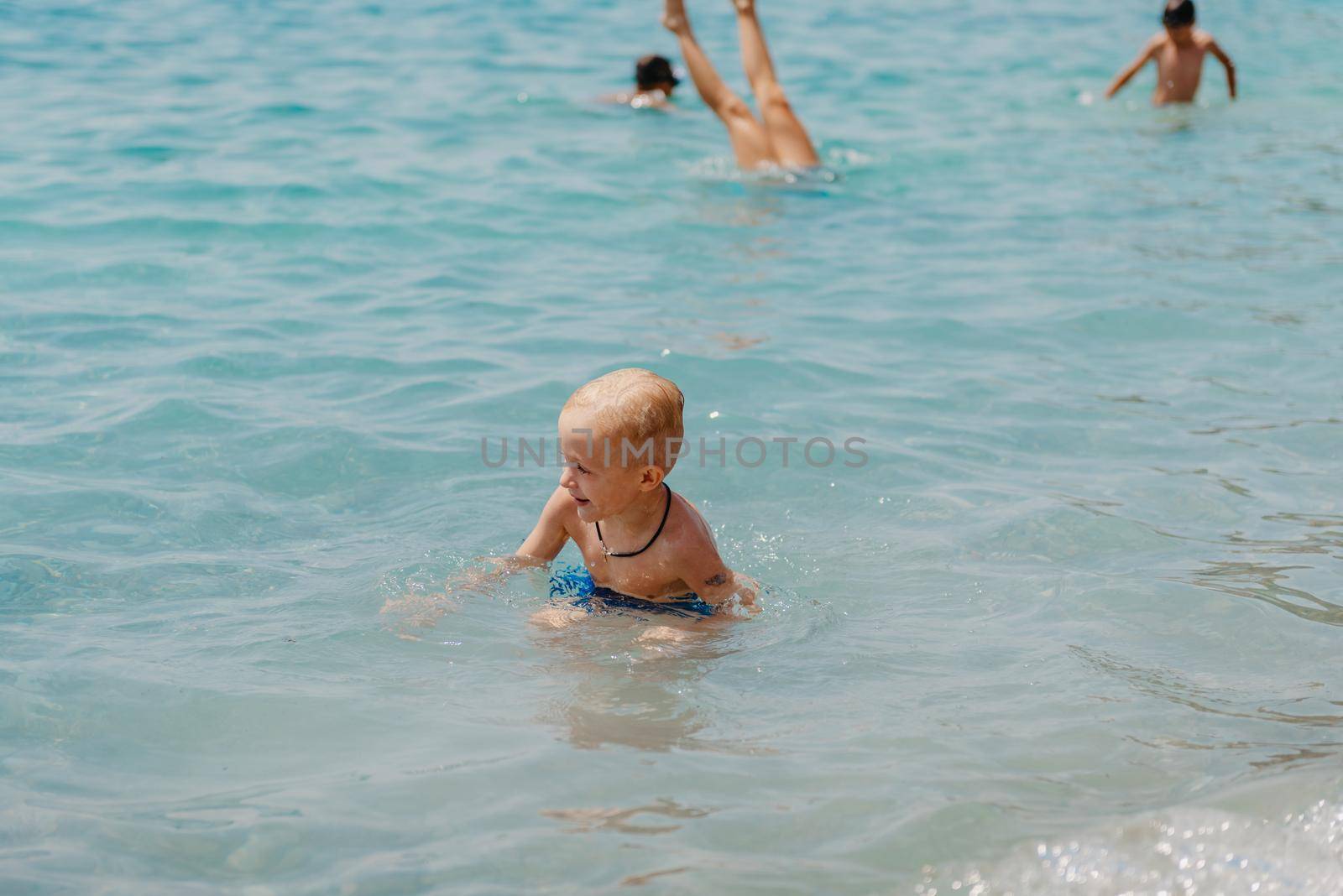 Child learning to swim in the open sea of tropical resort. Kids learn swimming. Exercise and training for young children. Little boy with colorful float board in sport club. Swimming baby or toddler. Happy child boy swims in sea in swimming circle with splash. Blue sky and water. Swimming training. Fun joy activities on vacation in the beach. Childhood moments lifestyle. Freedom careless. boy swim in the sea by Andrii_Ko