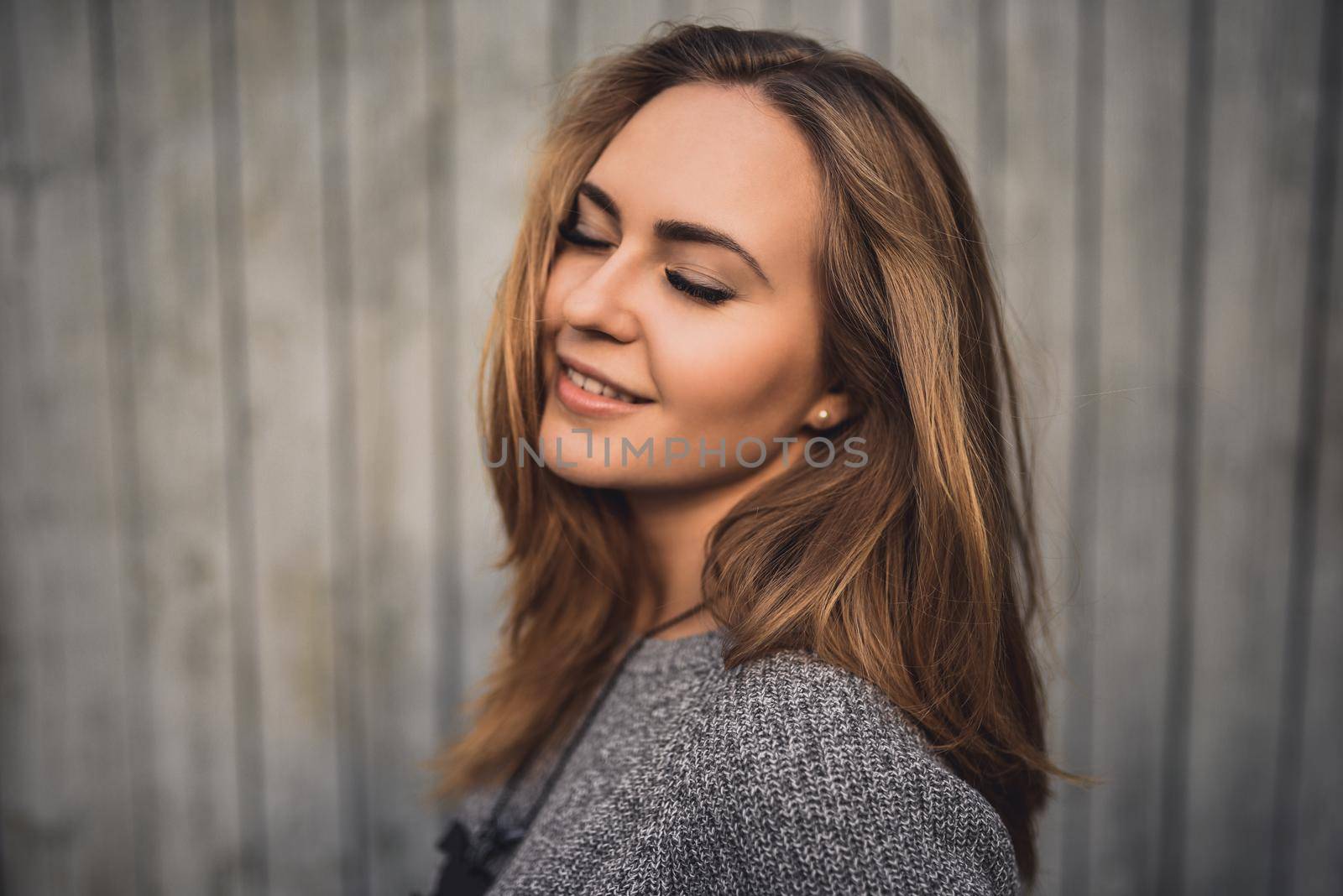 beautiful young blonde model girl with eyes closed and smile. gray knitted sweater. On the Sunset. Portrait. best retouch. on the background of gray wooden boards